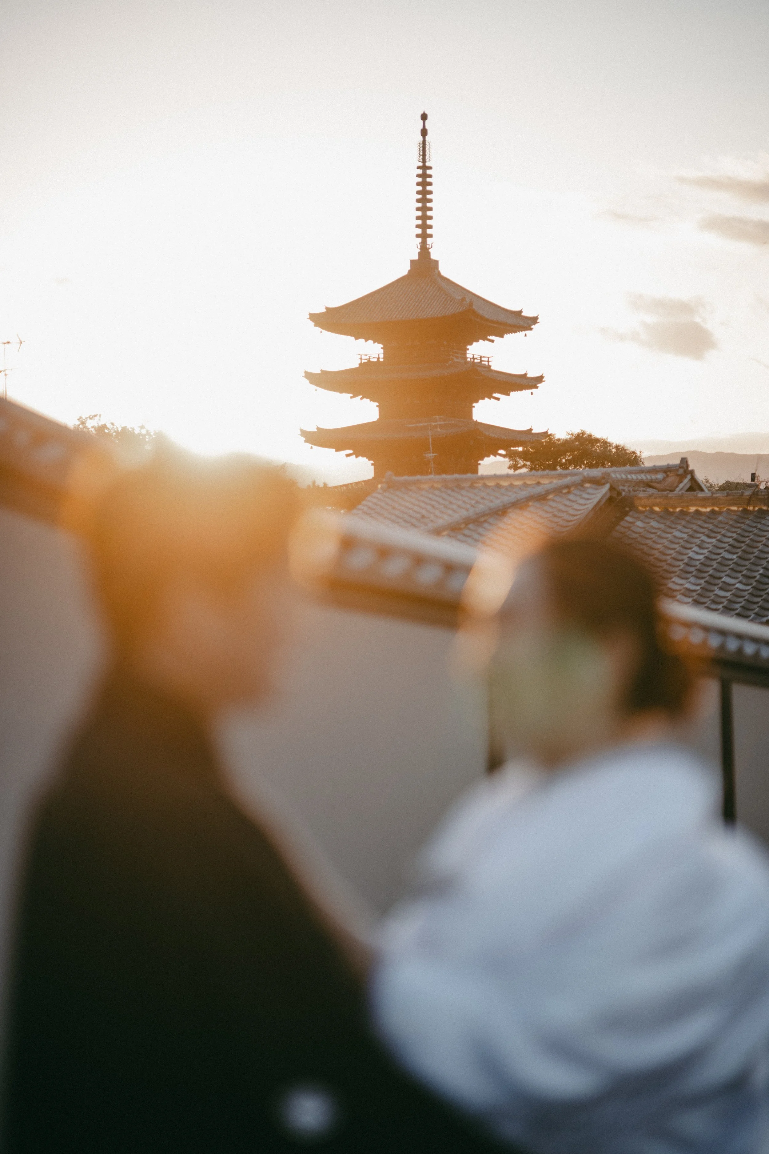 A pagoda silhouette at sunset, with blurred figures of two people in the foreground.