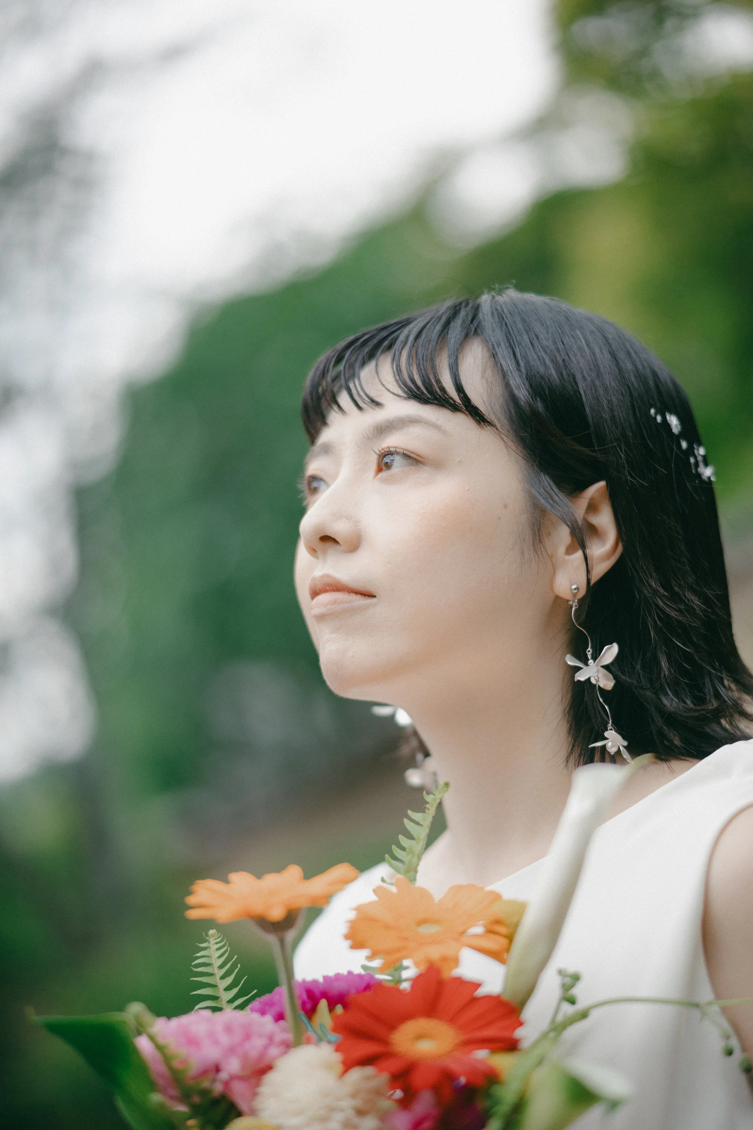 Woman with short black hair and butterfly earrings holding a bouquet of colorful flowers outdoors.