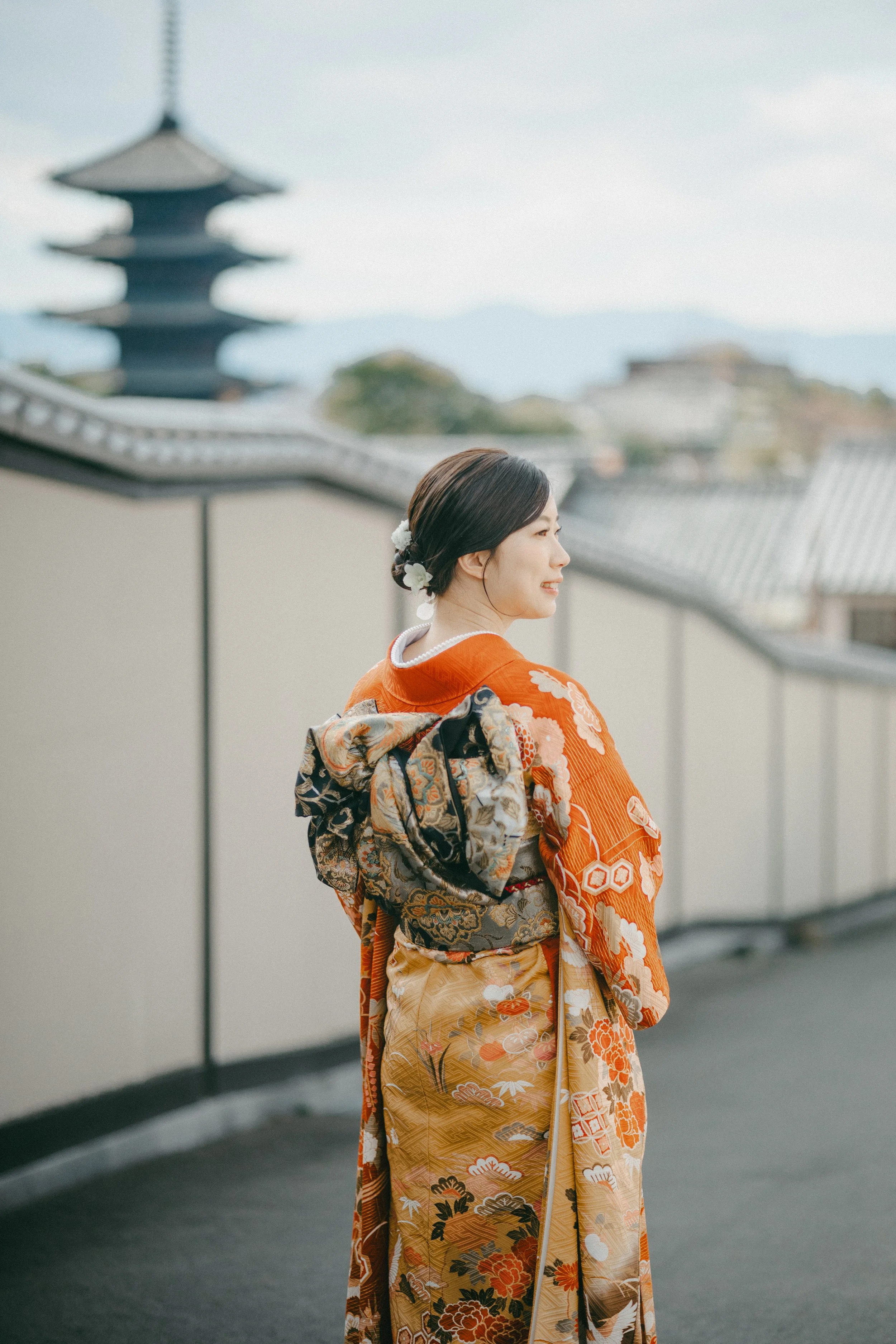 Woman in traditional Japanese kimono standing outdoors with a pagoda in the background.