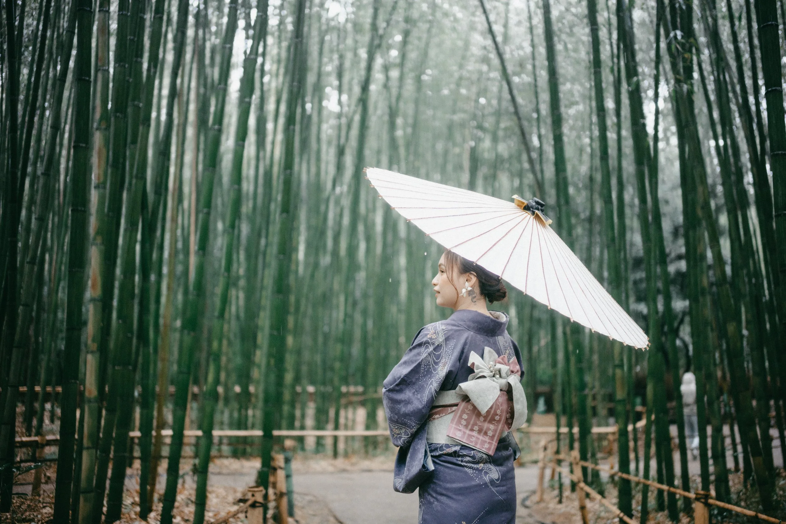 A woman wearing a traditional Japanese kimono holding a white umbrella in a bamboo forest.