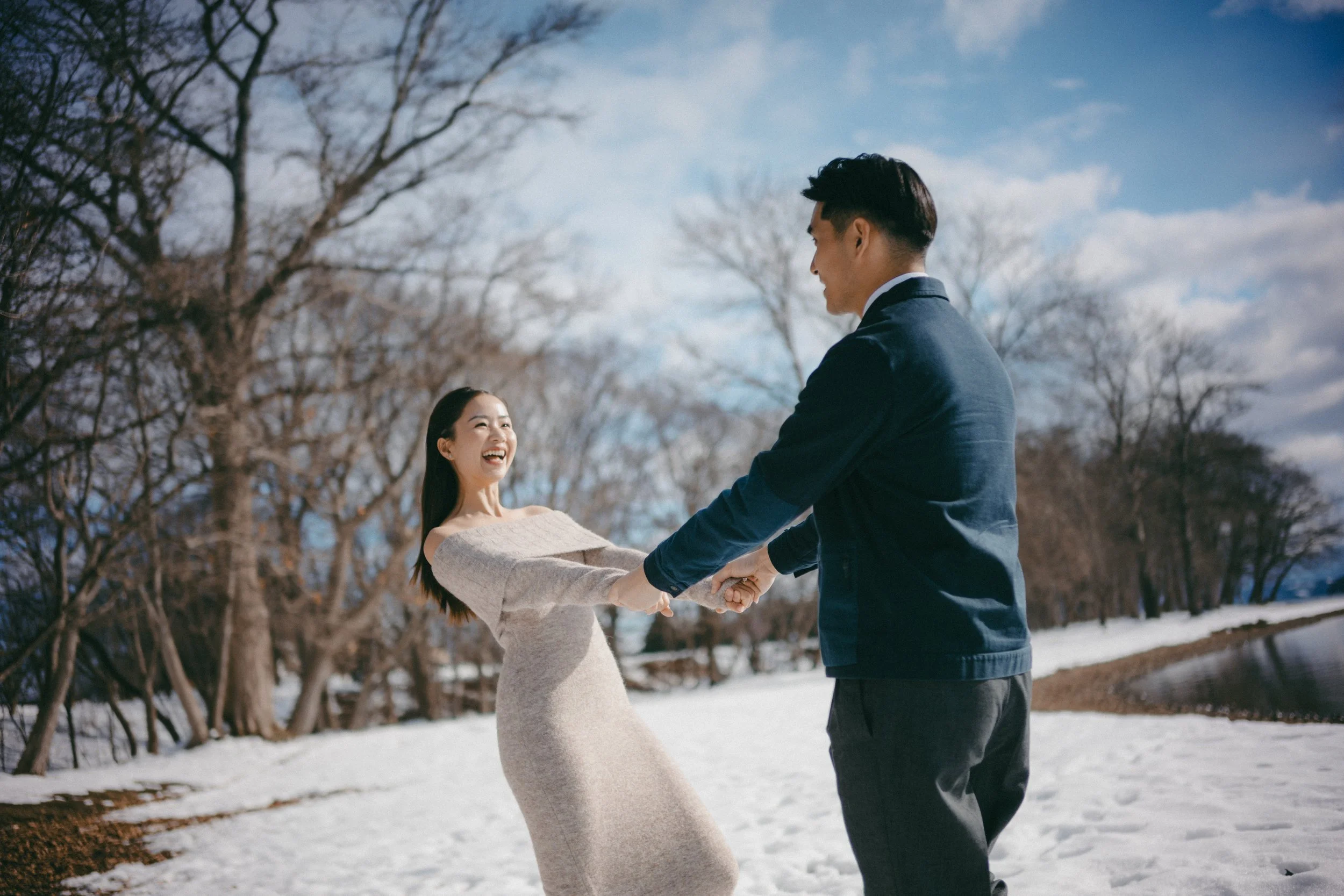 A couple is dancing outdoors in a snowy park, holding hands and smiling at each other.