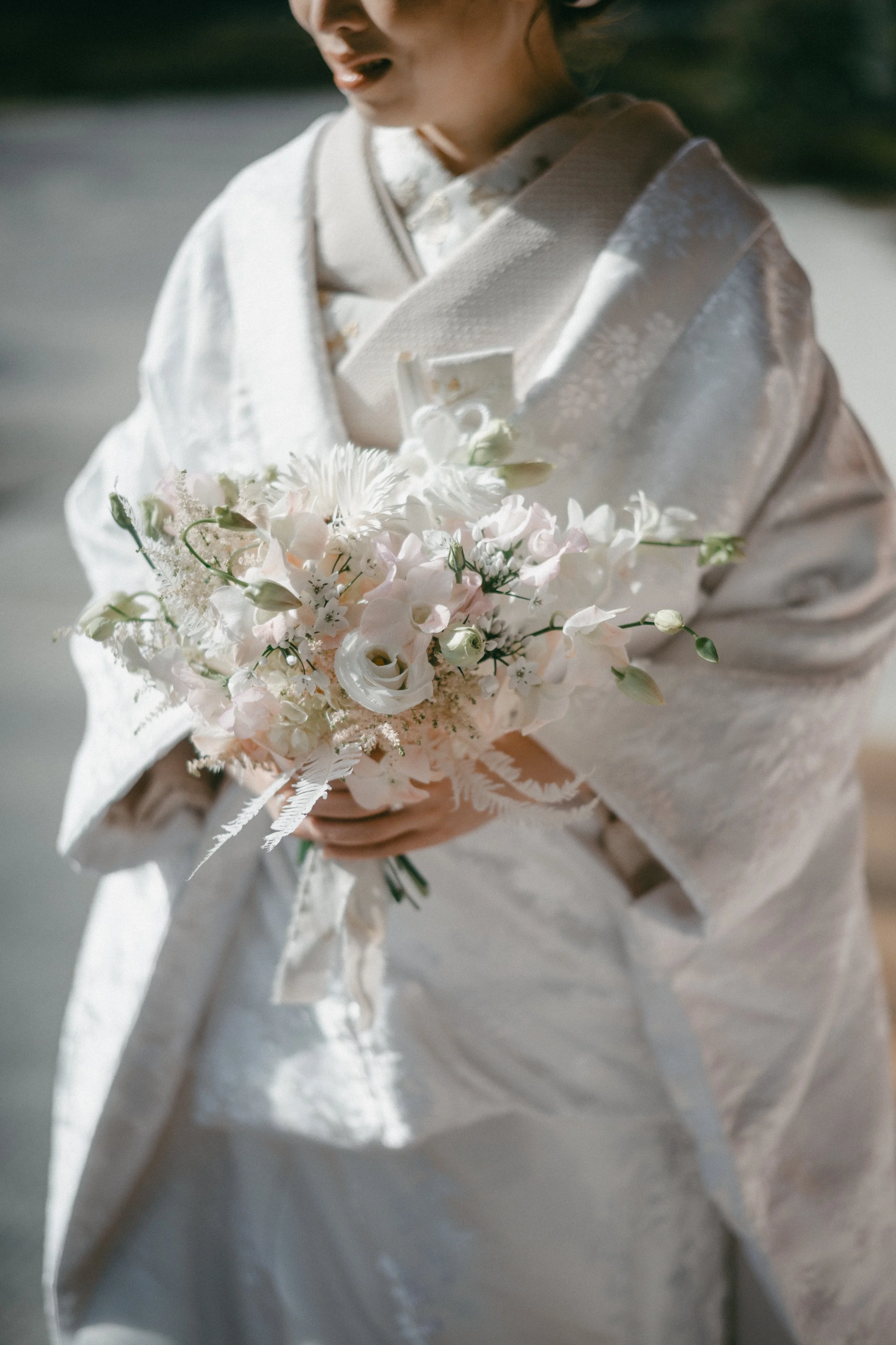 Person dressed in traditional white wedding attire holding a bouquet of white and pale pink flowers.