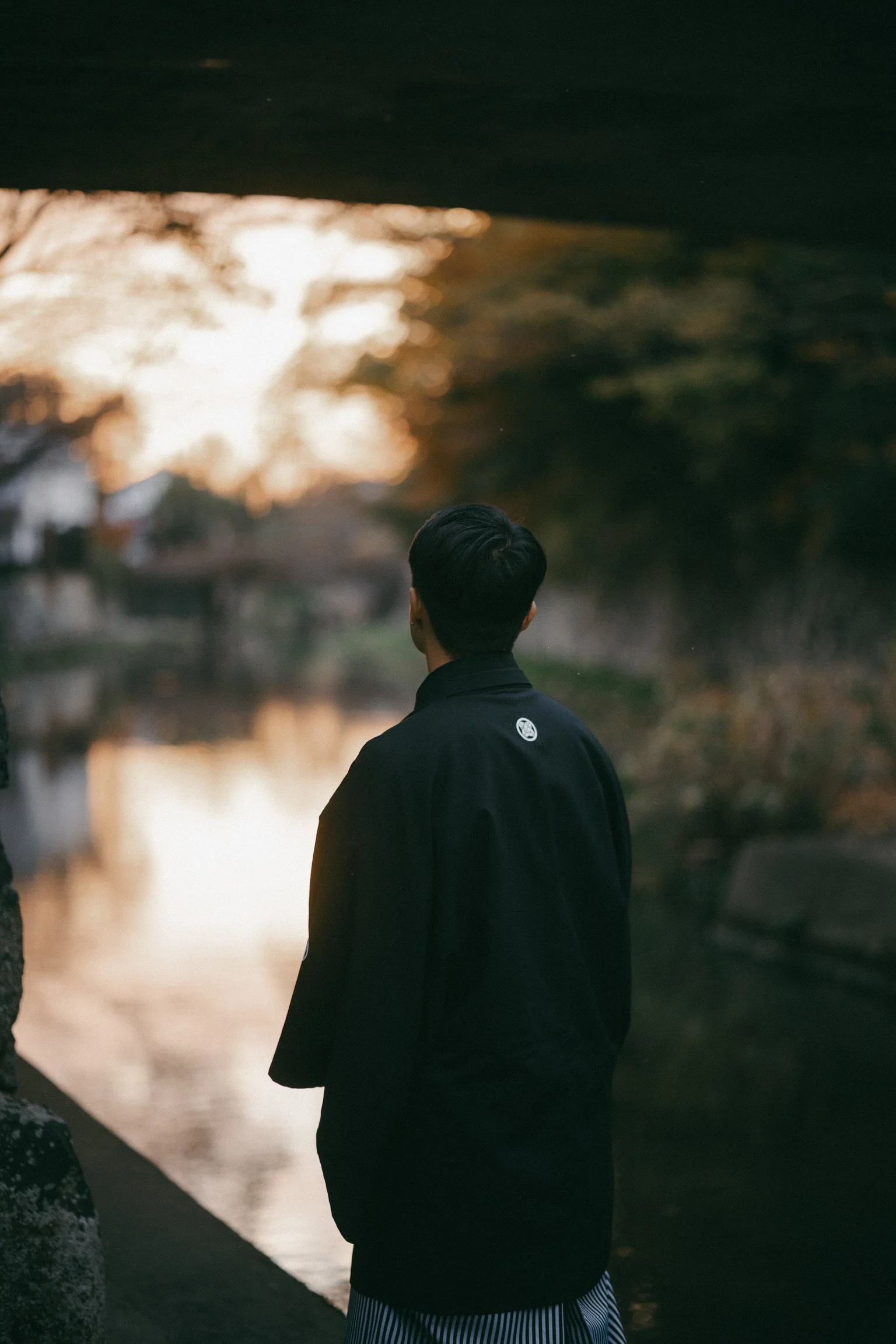 Person in black jacket standing by a river at sunset