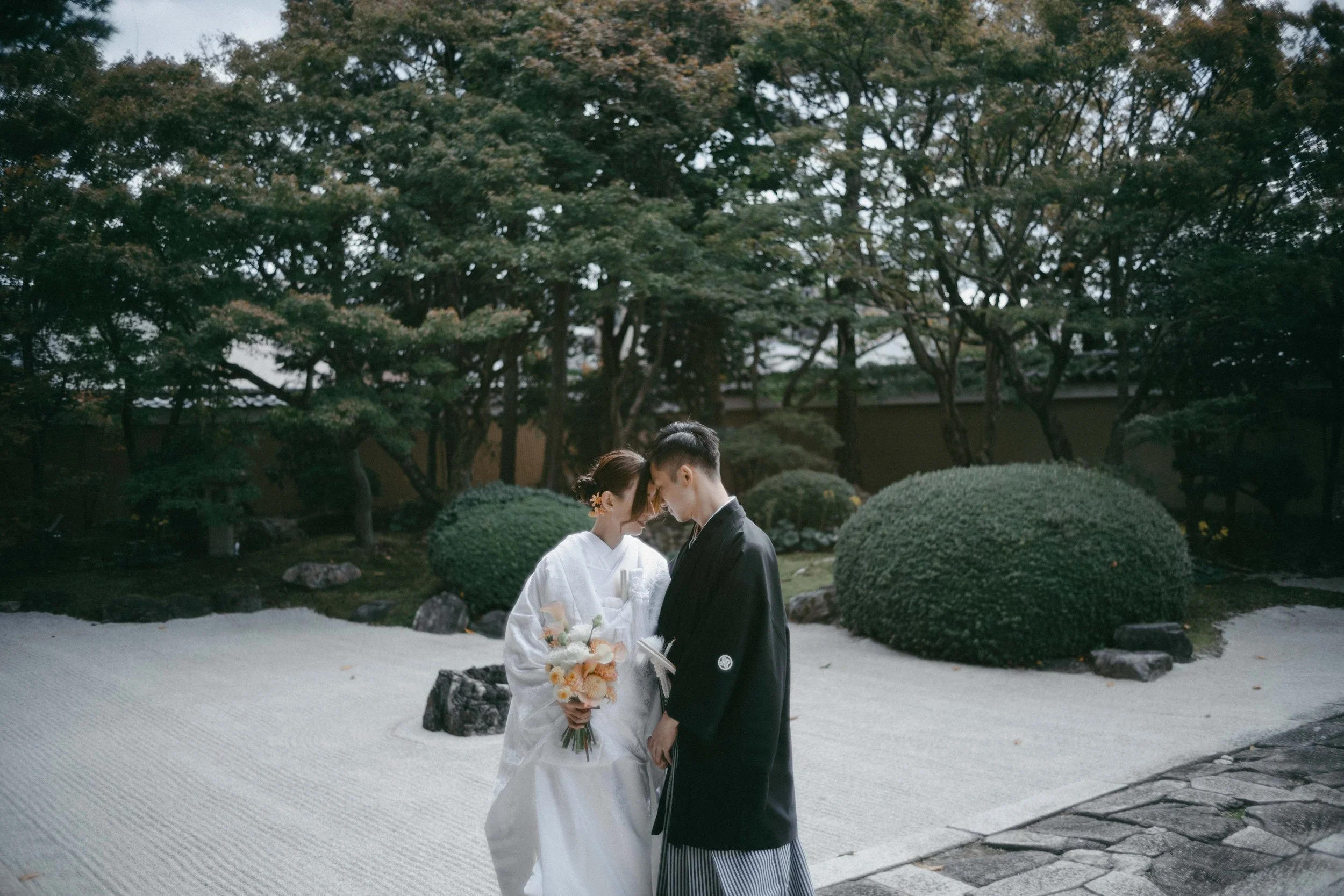 A bride and groom in traditional Japanese wedding attire sharing an intimate moment in a Japanese garden.