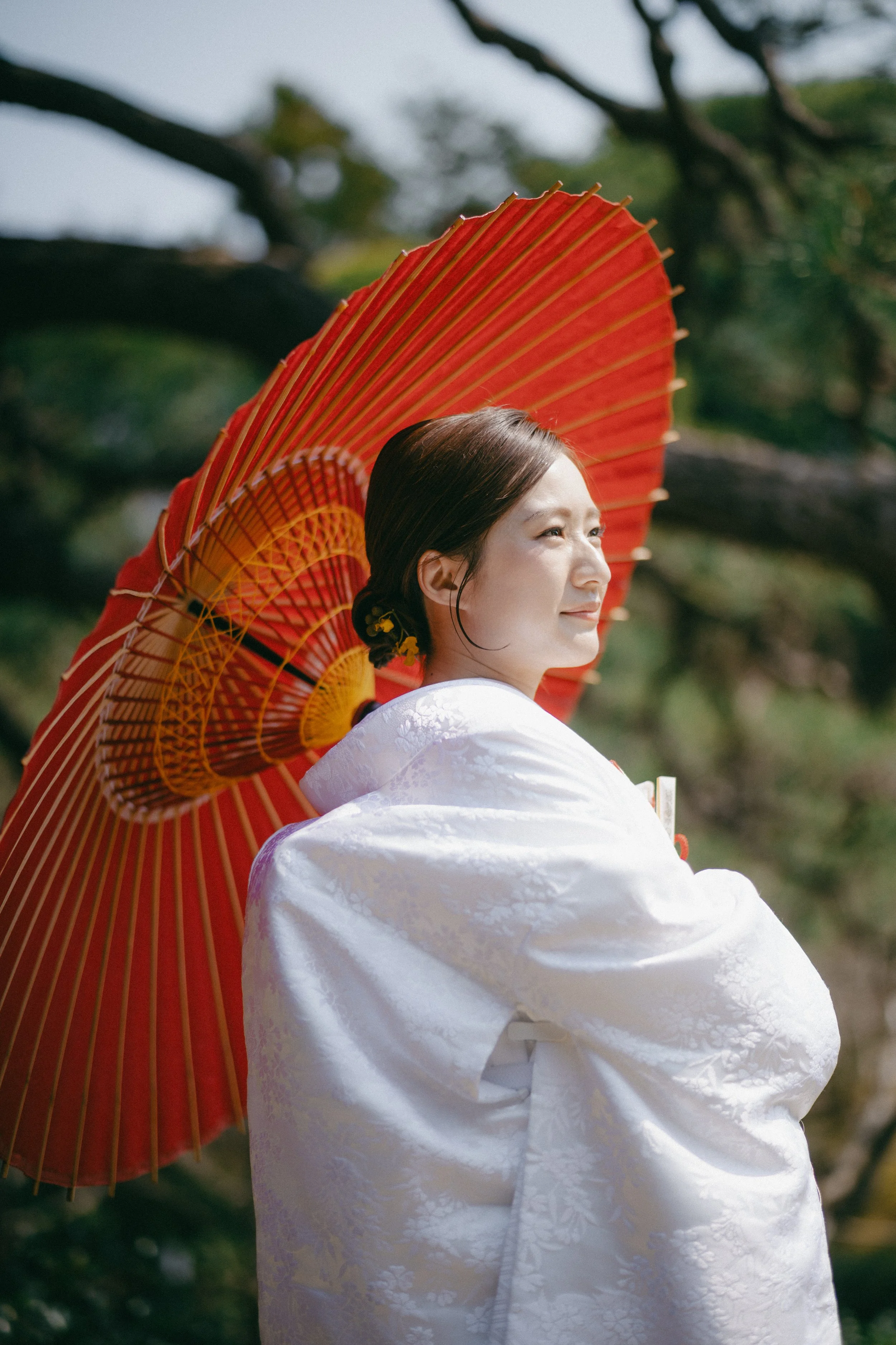 A woman dressed in traditional Japanese attire holding a red paper parasol outdoors.