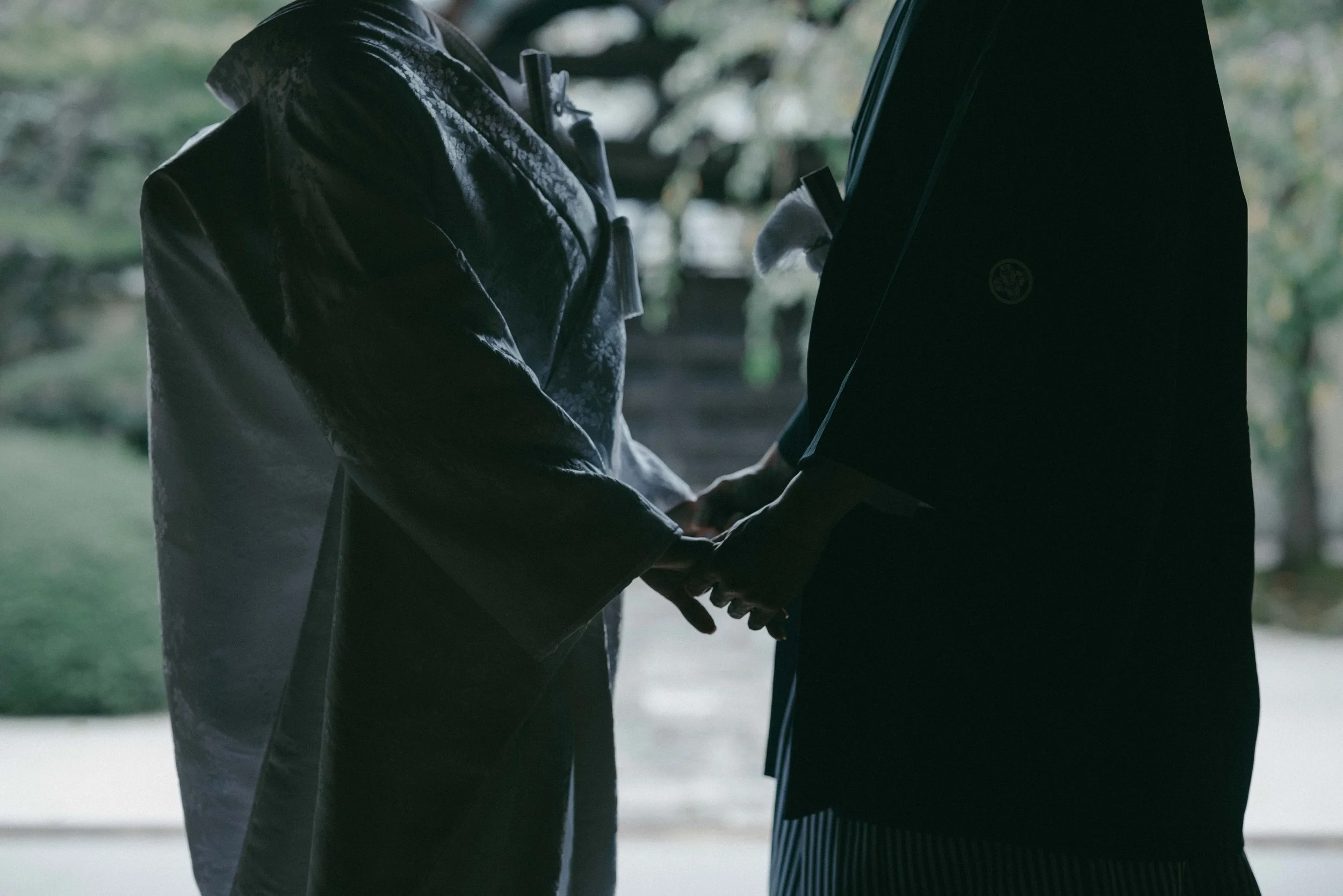 Two people holding hands in a silhouette against a blurred outdoor background.