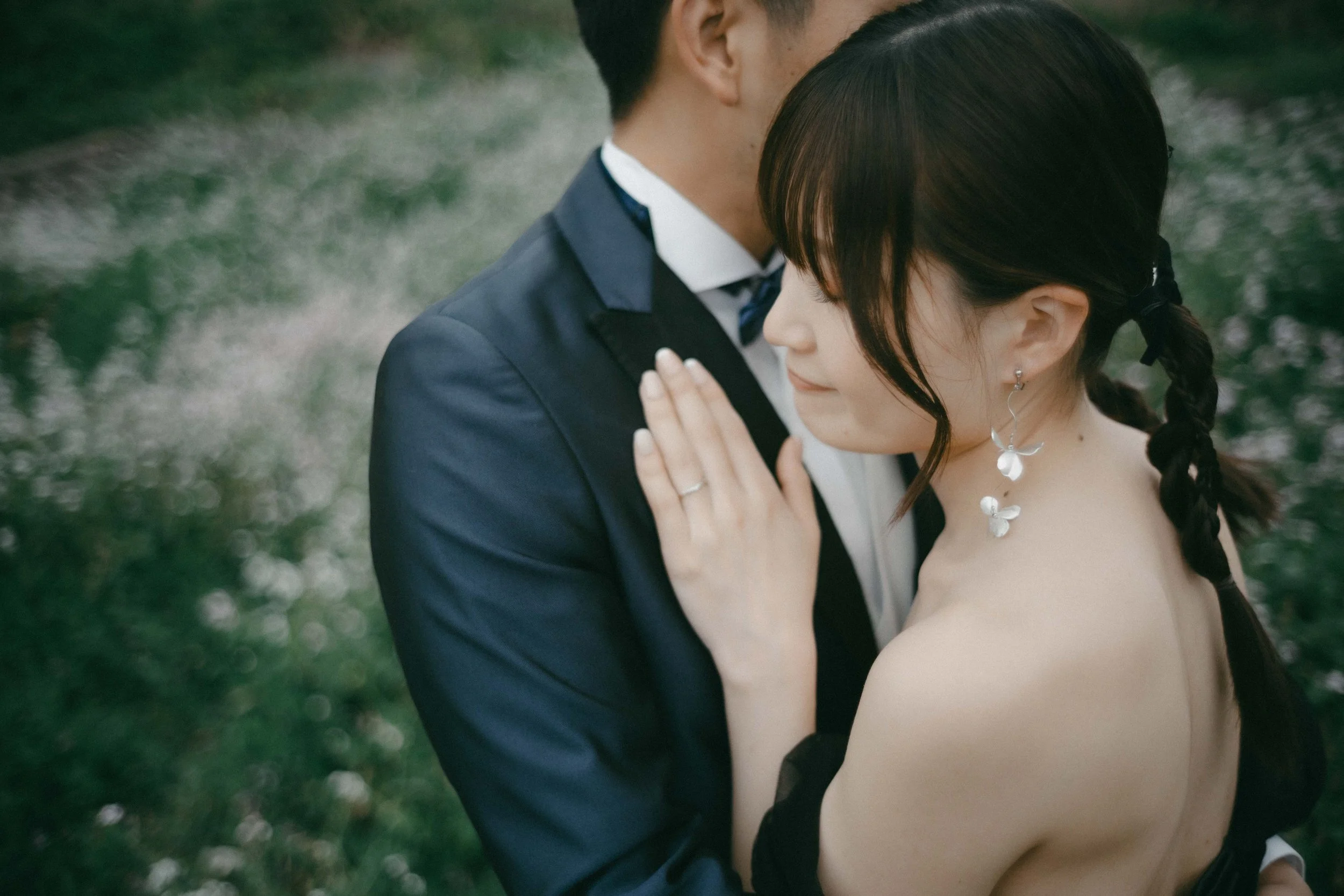 A couple hugging outdoors during what appears to be a wedding or romantic event, with the woman wearing butterfly earrings and the man in a suit.
