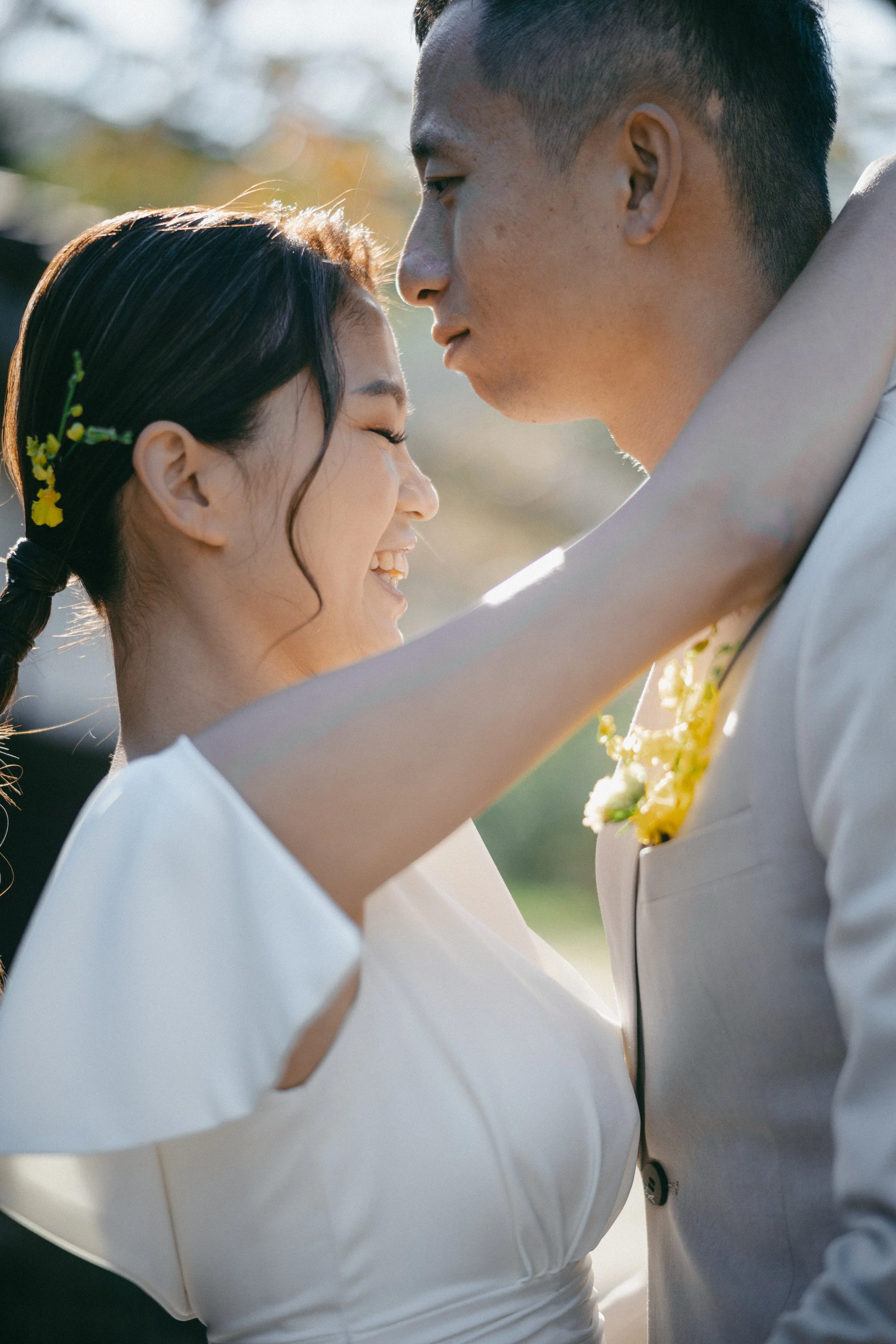 A happy couple on their wedding day, smiling as they hold each other close outdoors during daytime.