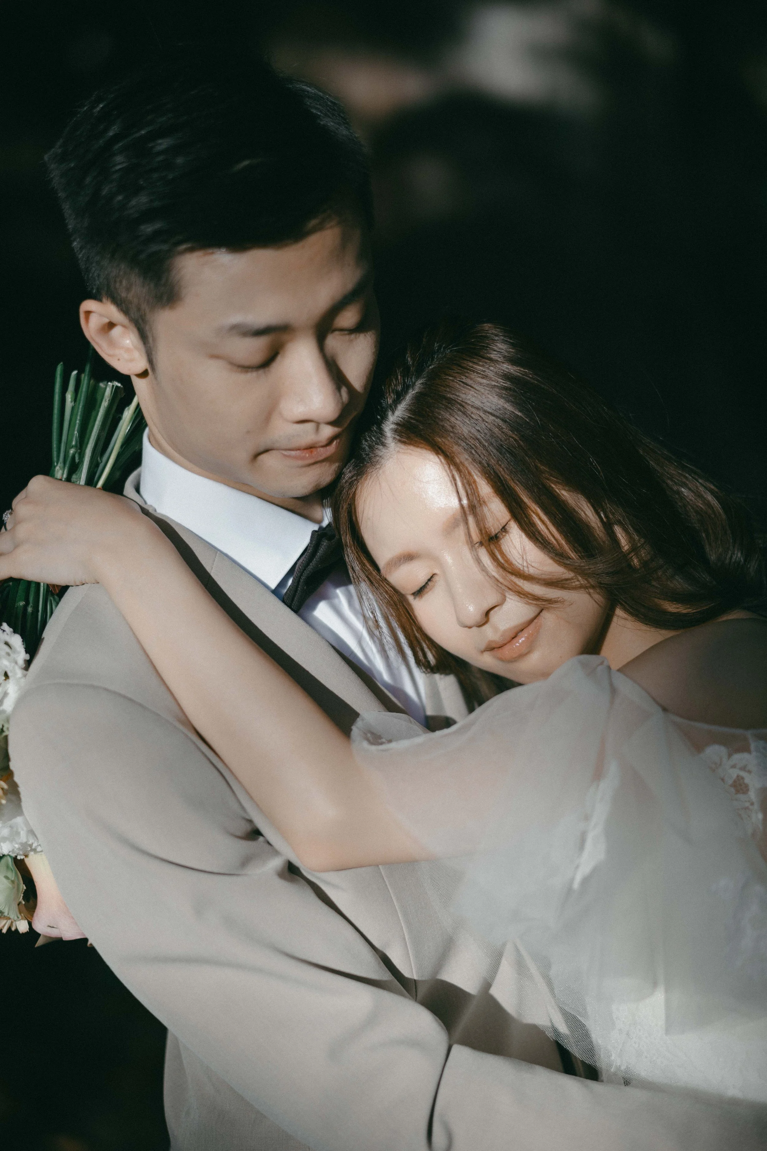 A man and woman embracing each other happily, with the woman resting her head on the man's chest and both having peaceful expressions.