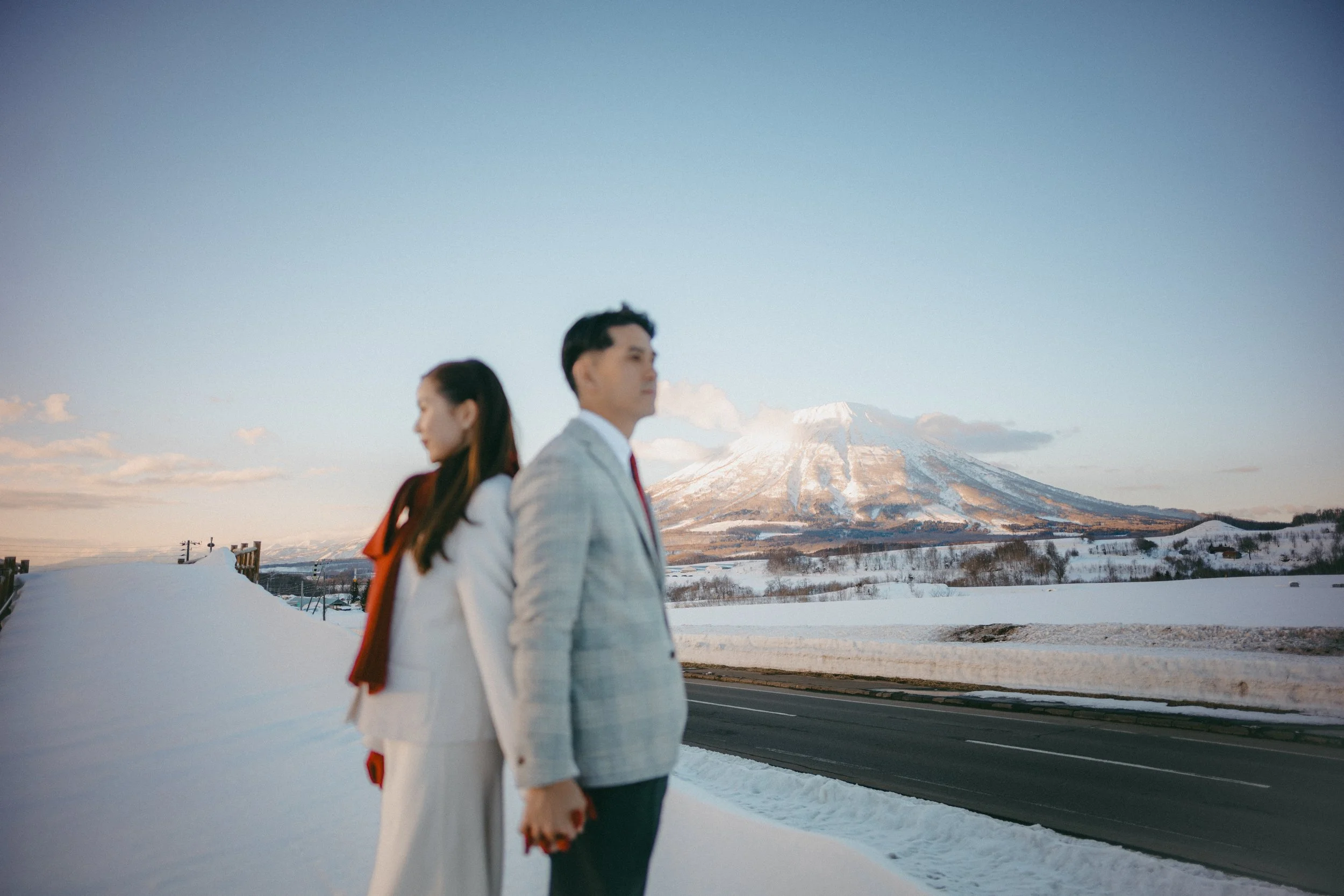 A man and woman in formal attire standing outdoors in a snowy landscape with Mount Fuji in the background.