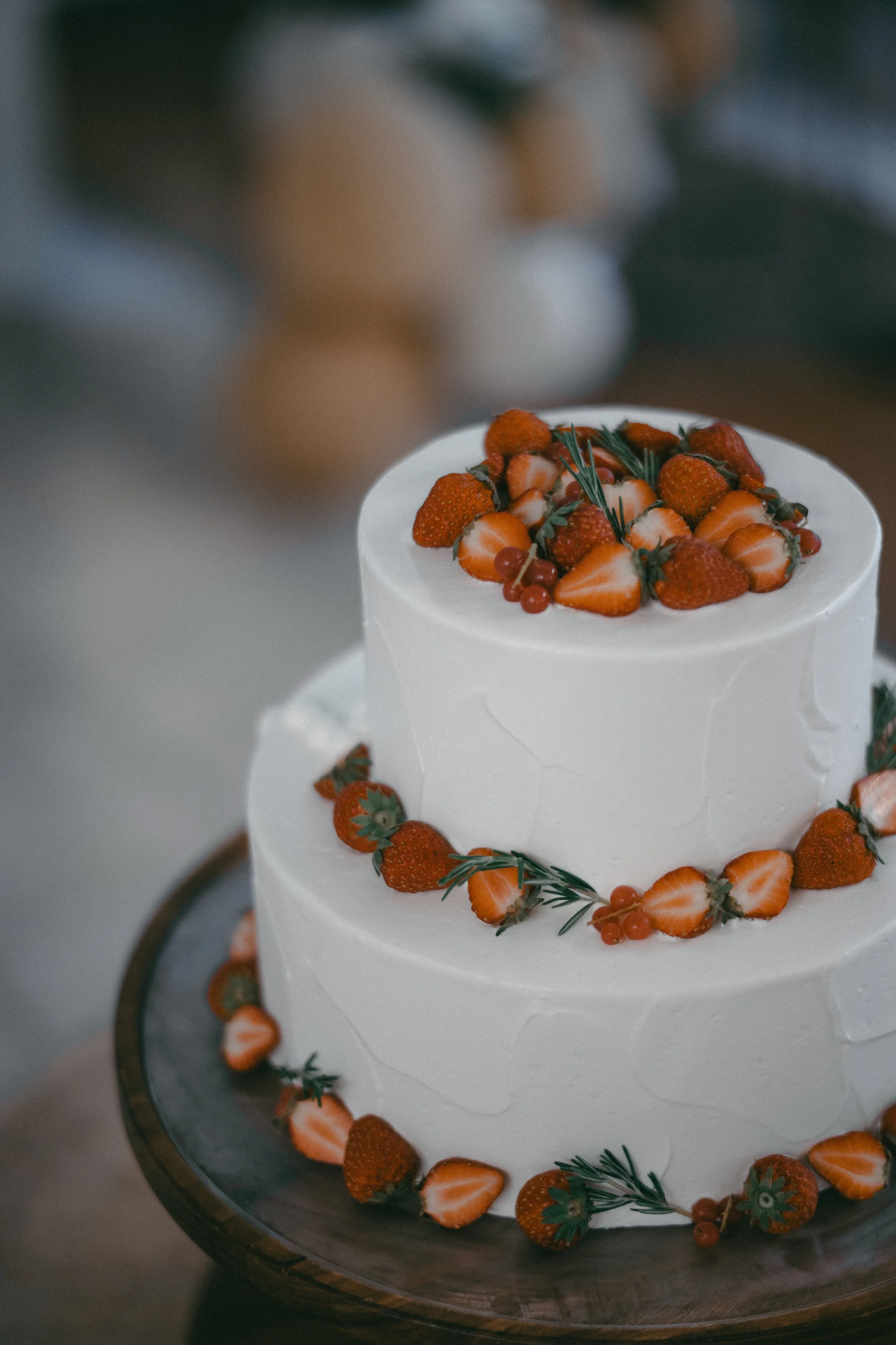 A two-tiered white wedding cake decorated with fresh strawberries, red currants, and sprigs of rosemary.
