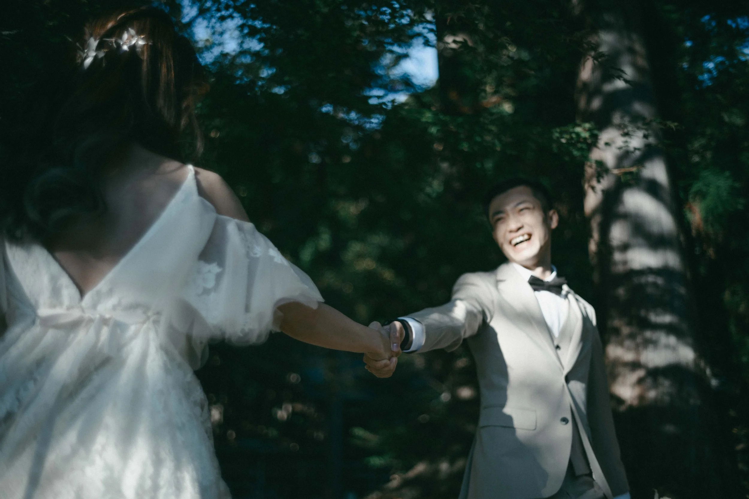 A newlywed couple holding hands and smiling in a wooded outdoor setting