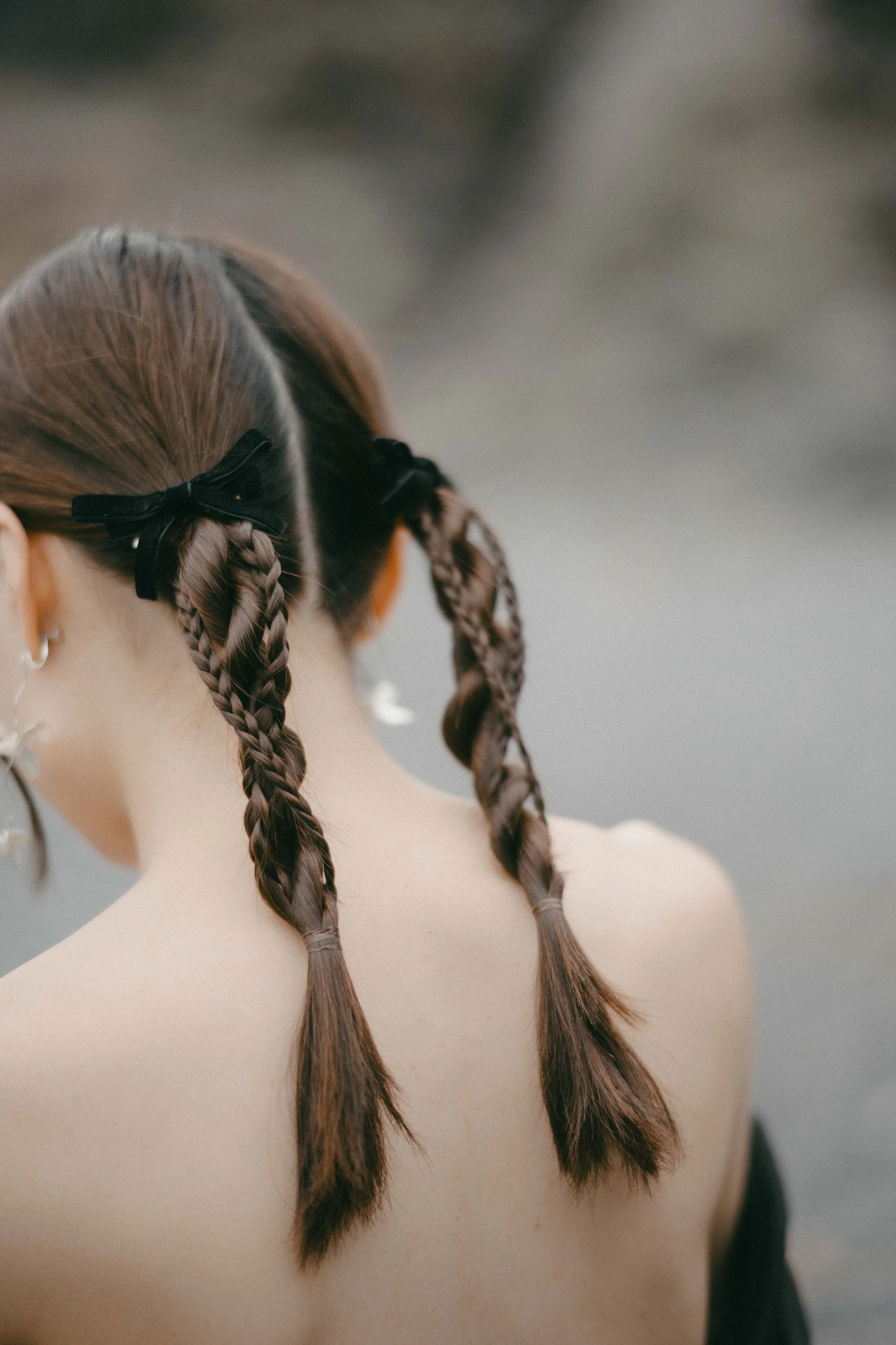 Back of a woman with braided hair, tied with black ribbon, outdoors near water.