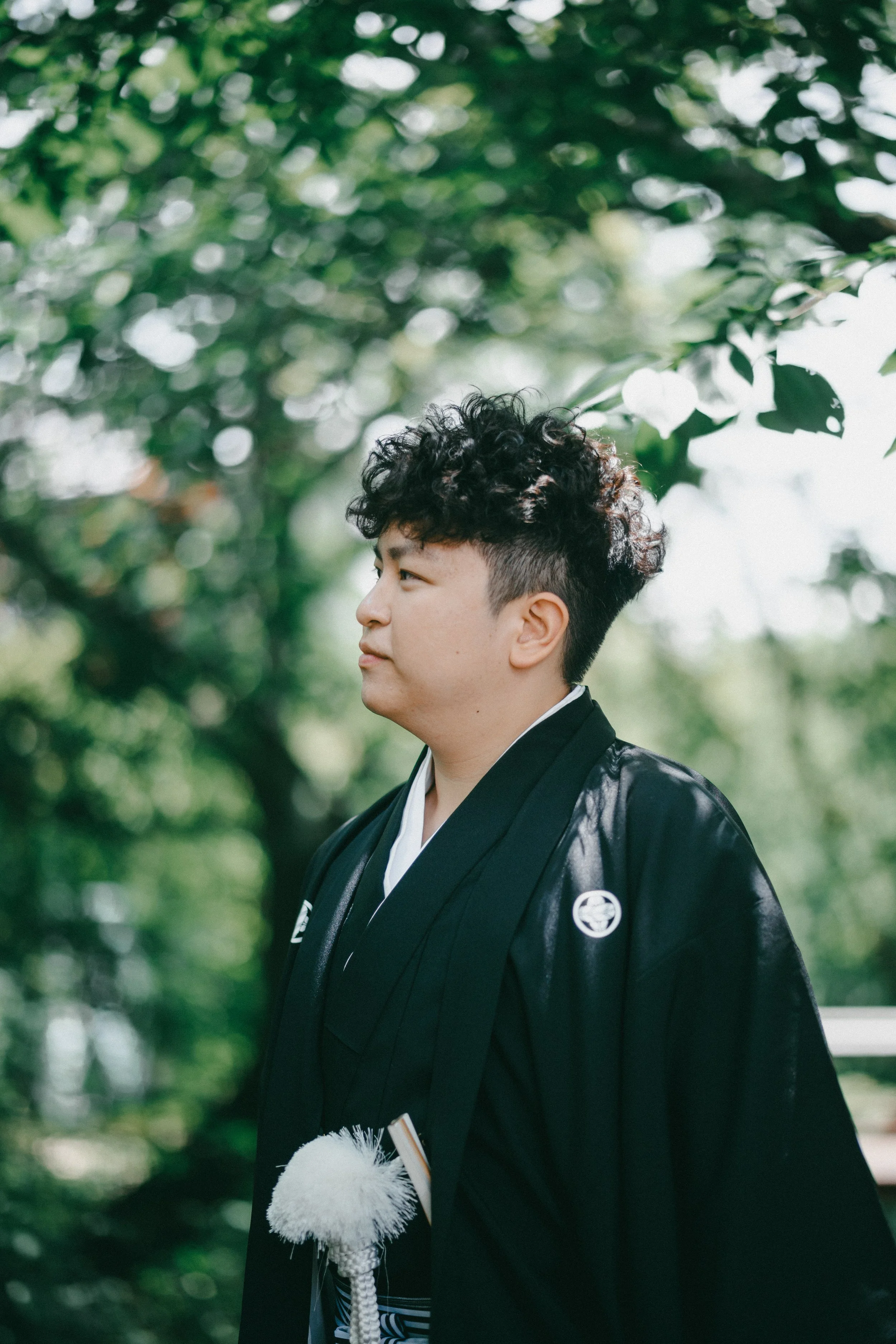 A young man in traditional Japanese attire standing outdoors with green trees in the background.