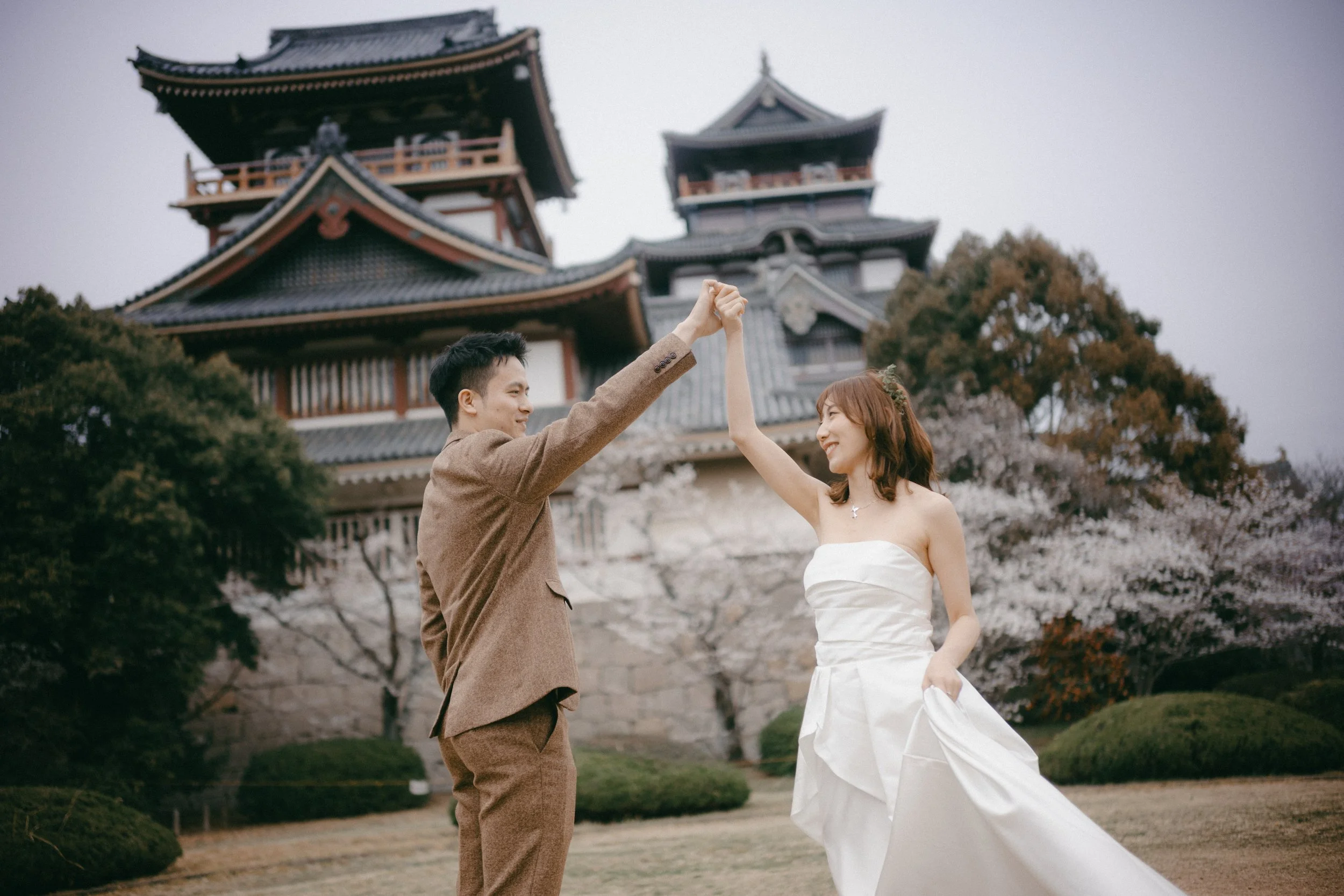 A newlywed couple dancing with a traditional Japanese temple and cherry blossoms in the background.