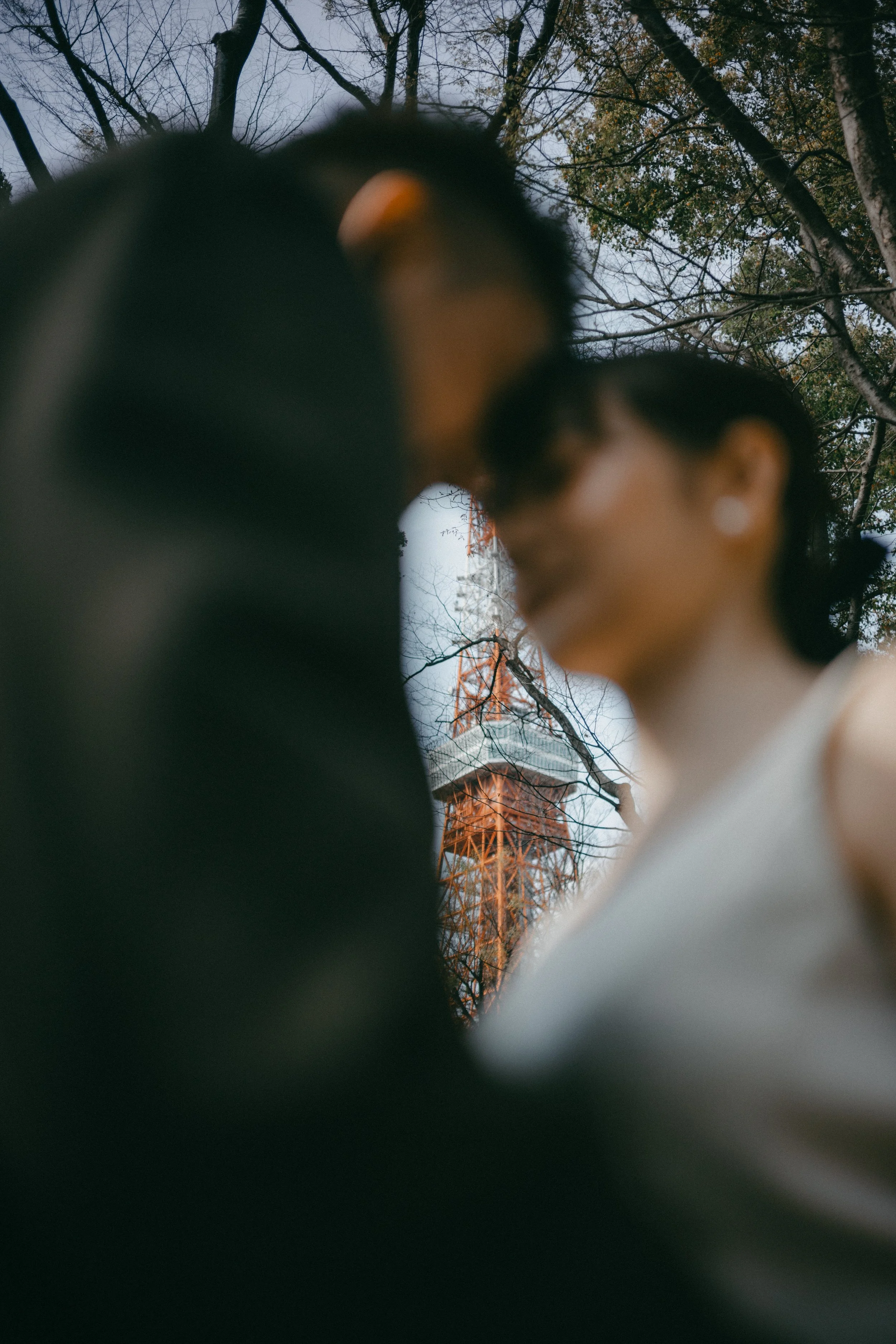A blurry photo of a couple with a tower in the background, surrounded by trees with fall foliage.
