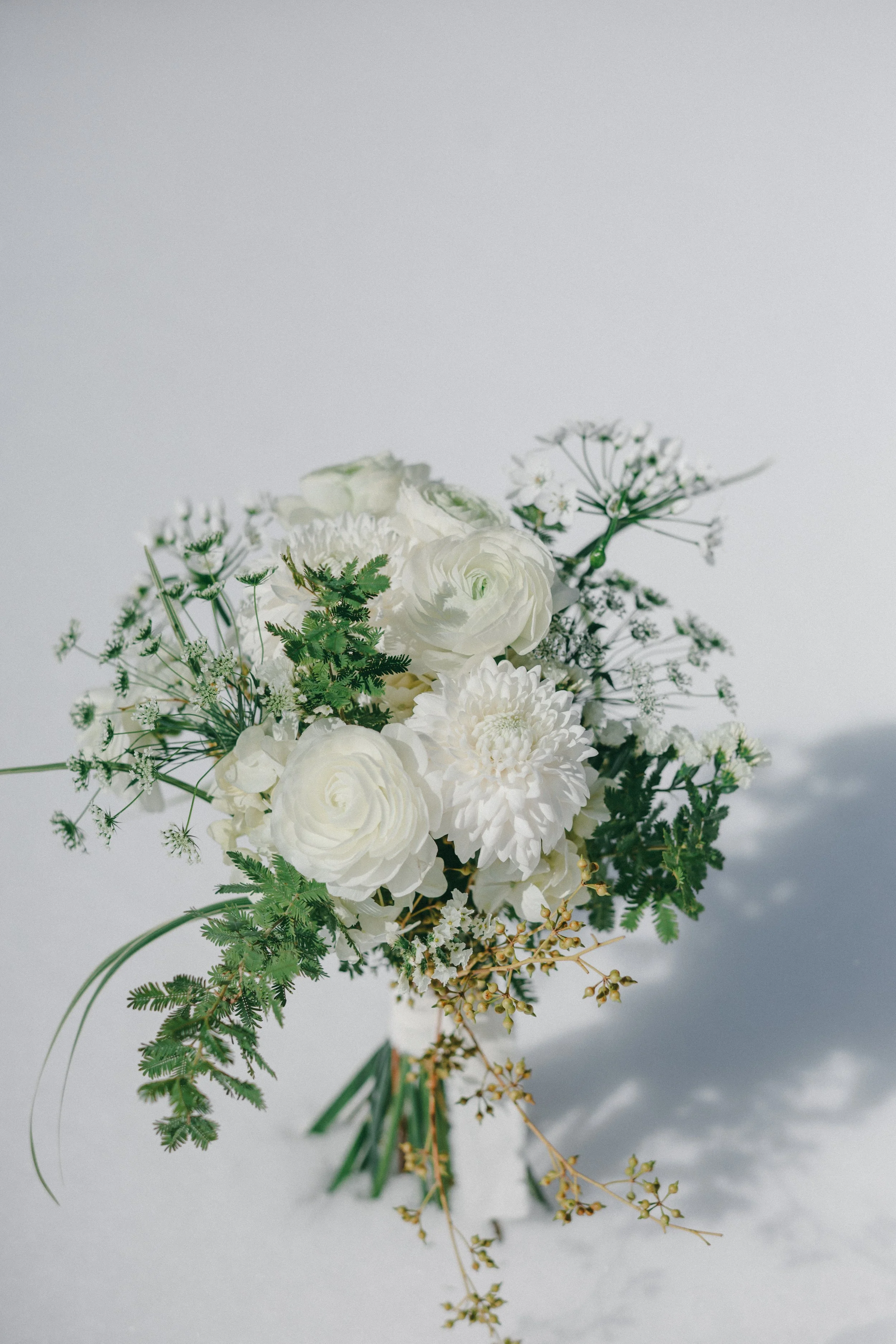 White floral bouquet with various flowers and greenery placed on a white surface.