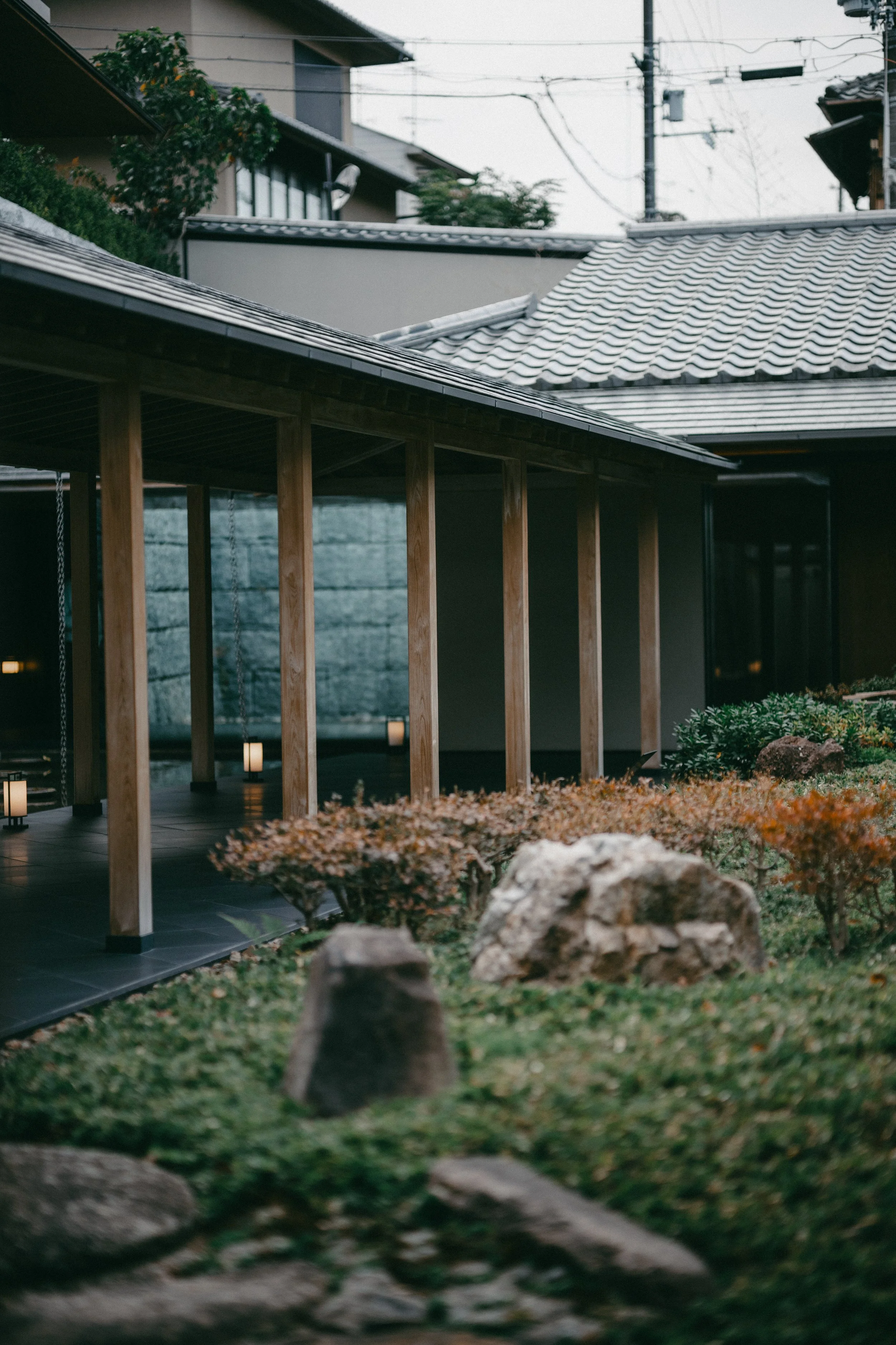 A Japanese-style building with a tiled roof, wooden pillars, and a garden with rocks and shrubbery.