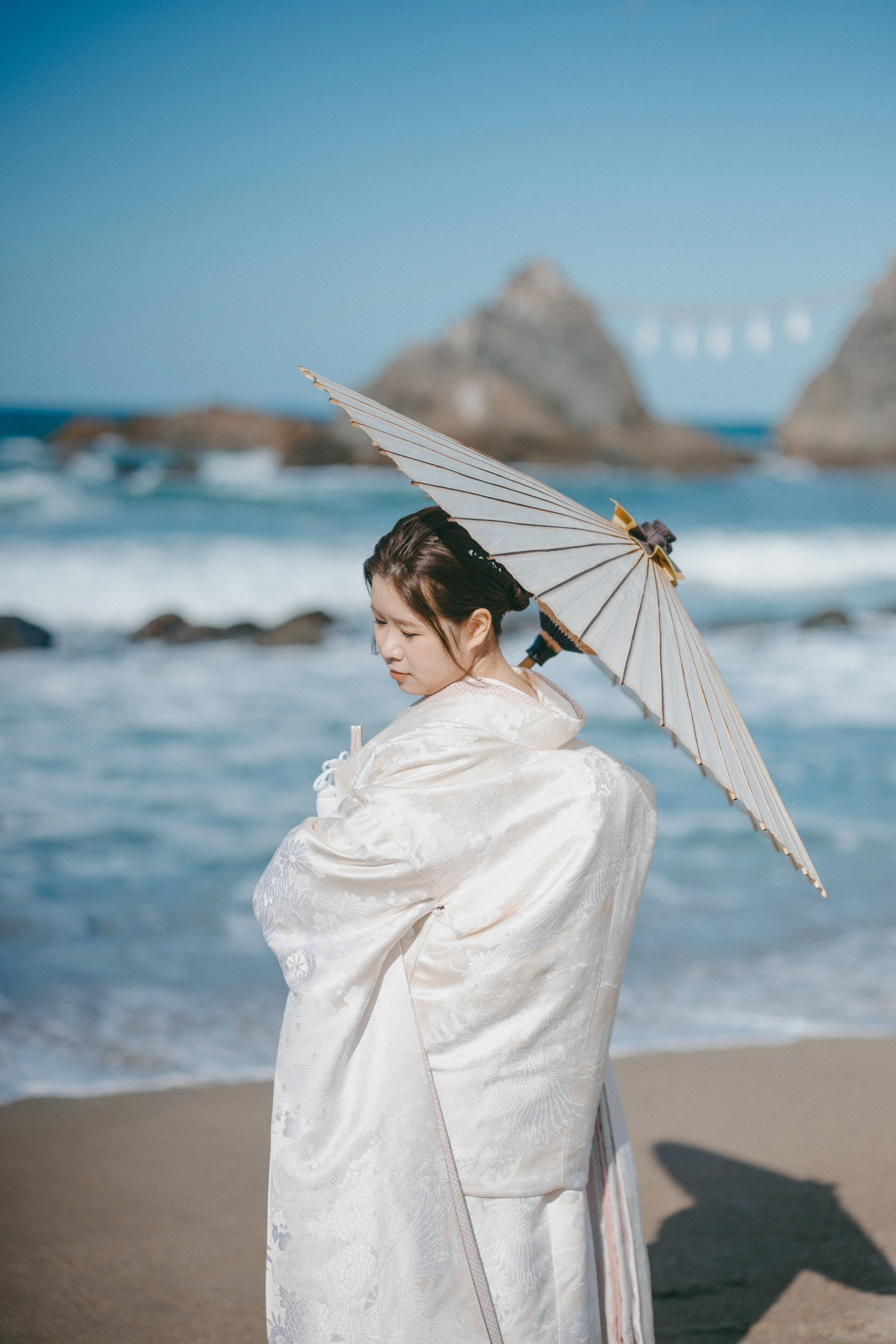 Woman in traditional Japanese kimono with white parasol on beach.