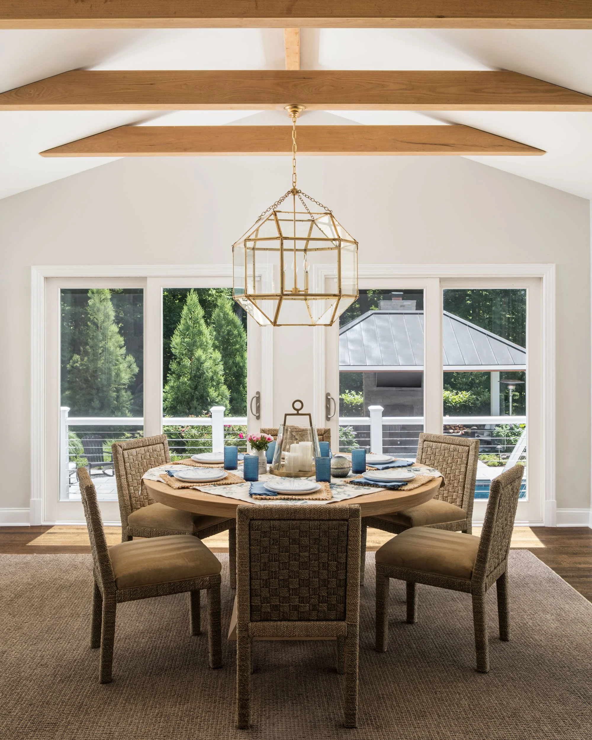 Dining room with round table, wicker chairs, and large geometric chandelier, featuring glass doors opening to outdoor view.