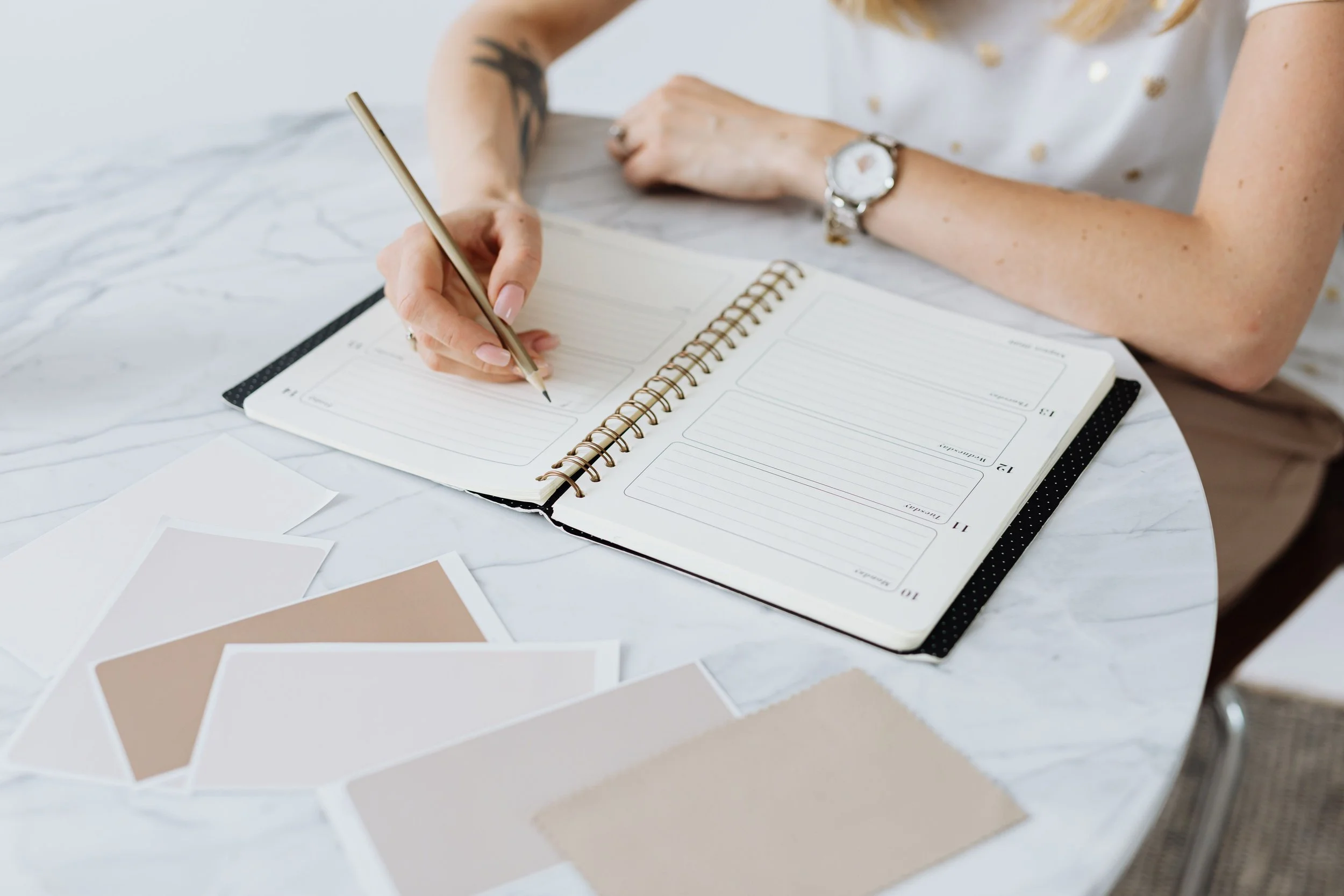 A person writing in a planner with color swatches and color samples on a white marble table.