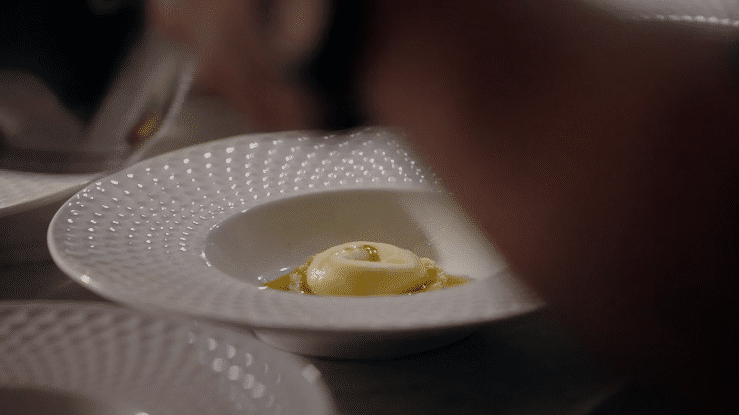 A small white bowl with a dotted pattern containing a scoop of vanilla ice cream with caramel sauce.