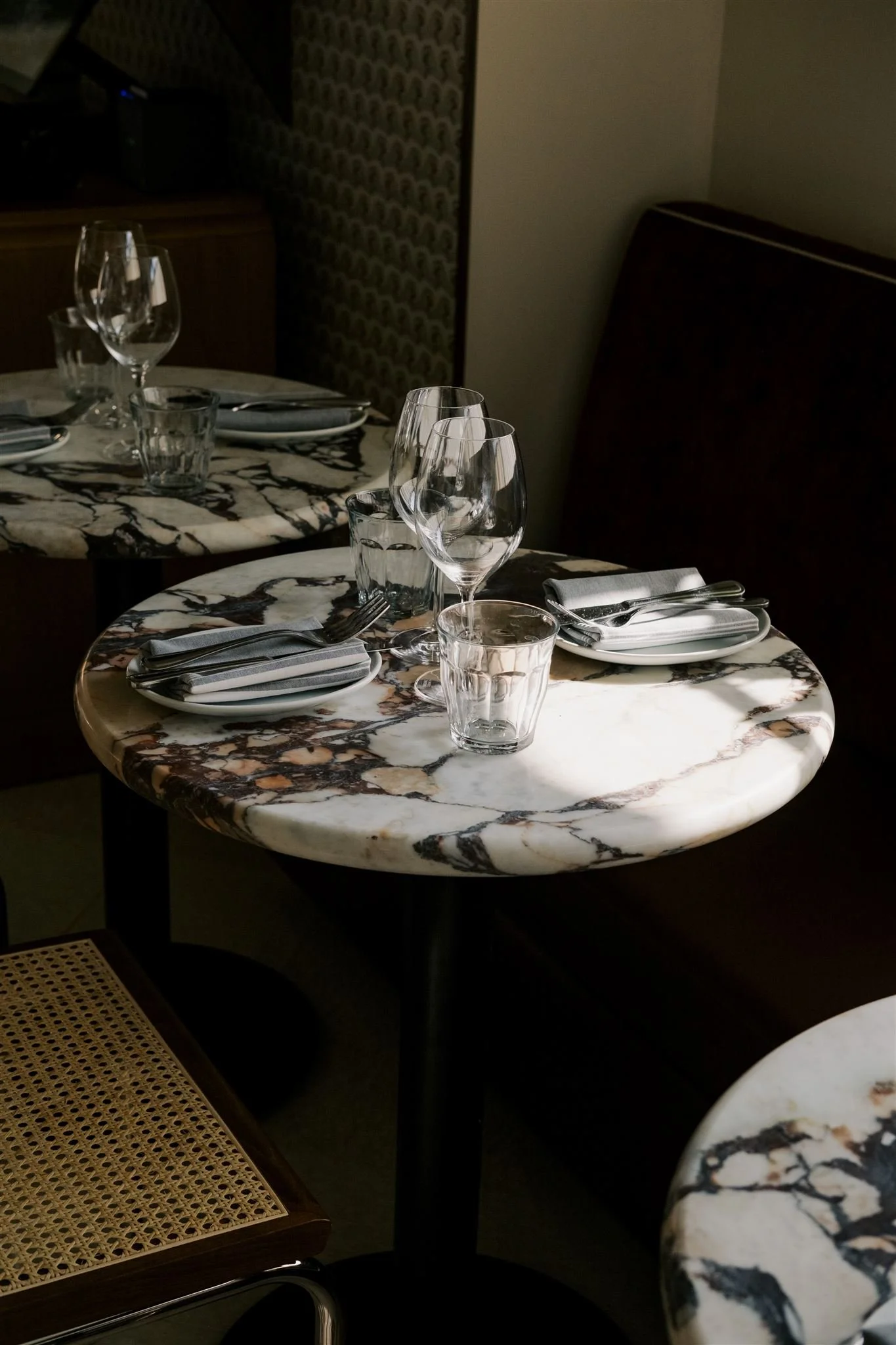 Elegant dining table set with glassware, silverware, and napkins on a marble surface in a dimly lit restaurant.