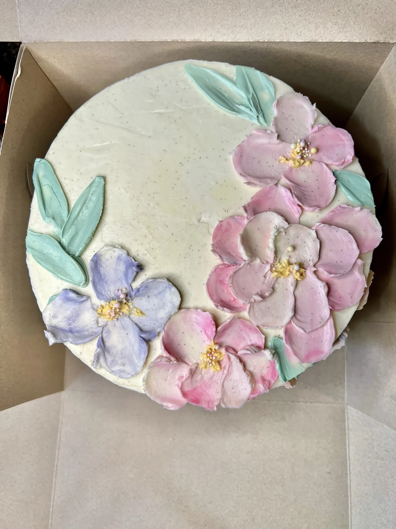 A round cake decorated with pastel pink, purple, and green floral frosting 