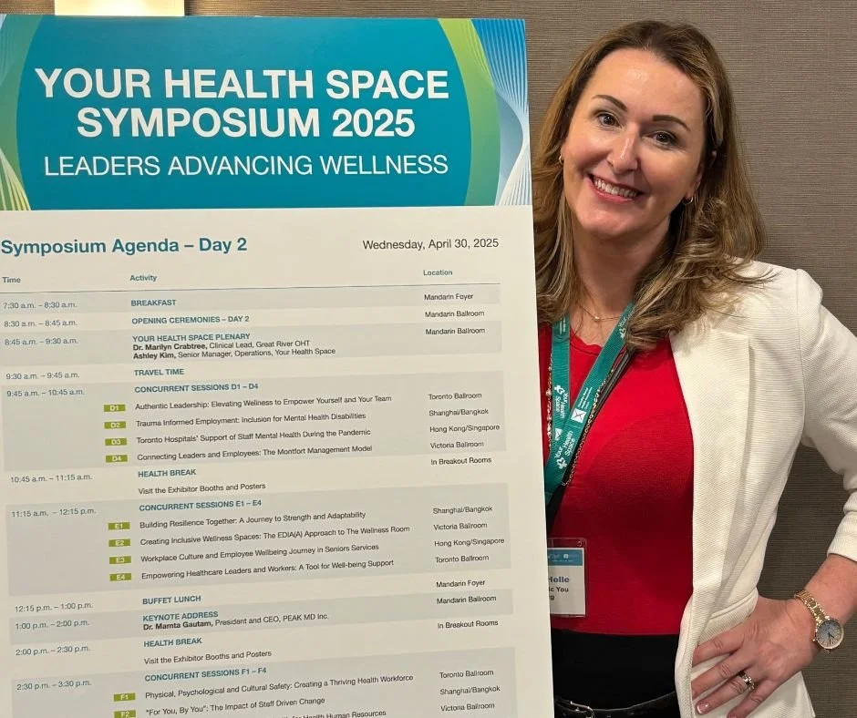 Kristina Holle - speaker smiling and holding a large symposium agenda poster at the 'Your Health Space Symposium 2025'. The agenda includes activities and sessions scheduled for April 30, 2025, at various locations.