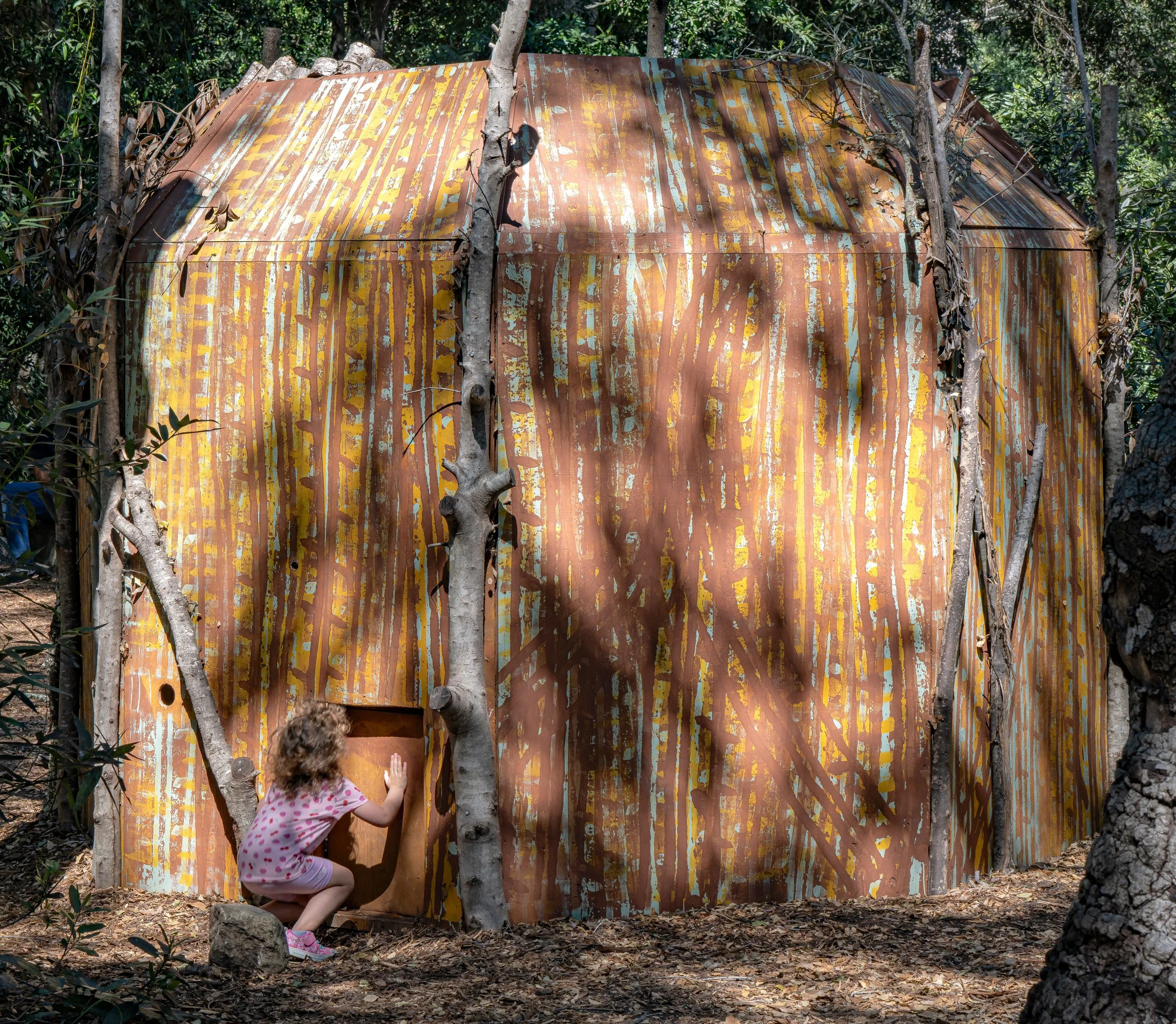 Girl pushes door on tree-painted structure.jpg