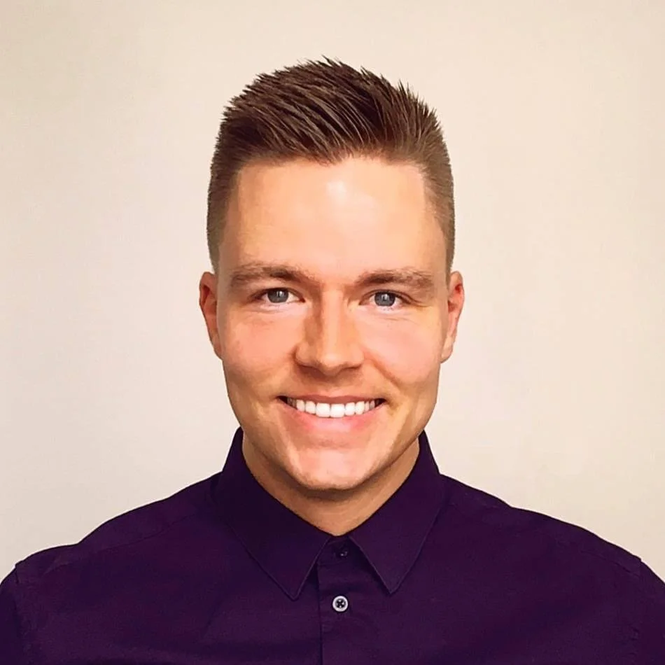 Smilende ung mand med kort, stylet hår iført mørk skjorte, fotograferet mod en neutral baggrund.