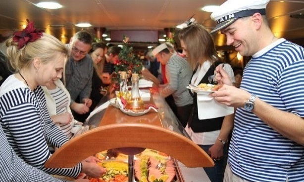 Group of people serving themselves food at a buffet, some in sailor hats and striped shirts, in a festive setting.