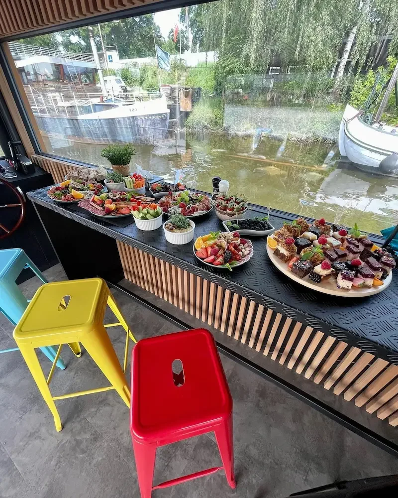 Assorted fruit desserts and snacks on boat on a river, with colorful chairs in the foreground.