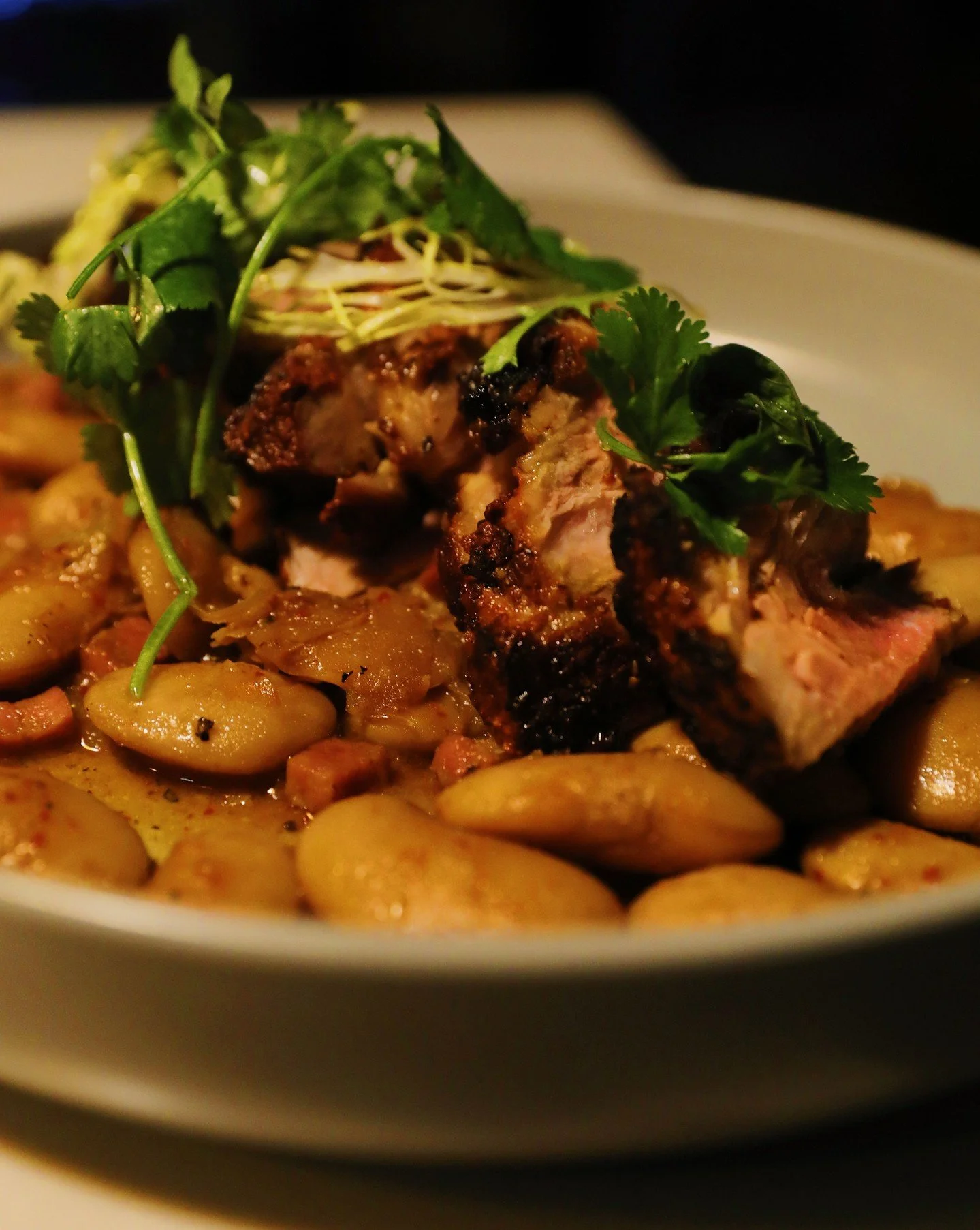 Close up: grilled pork shoulder in the soft glow of the bar. 

Join us for happy hour at the first and last hour of service at the bar everyday!