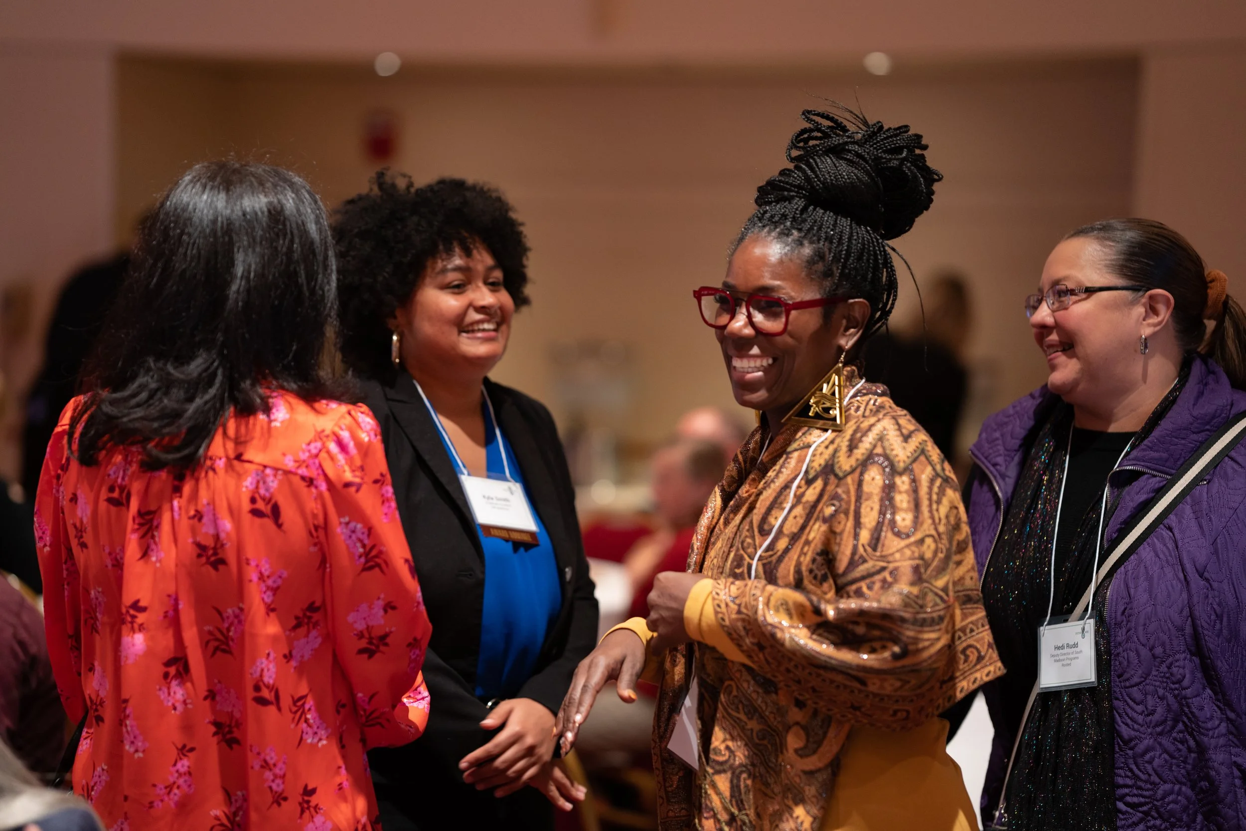 Four women smiling and talking at a conference.