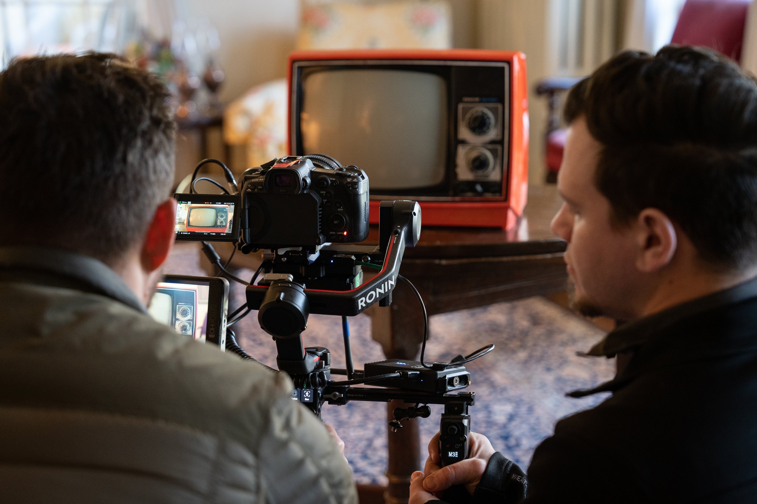 Two men filming a vintage television, indoors.