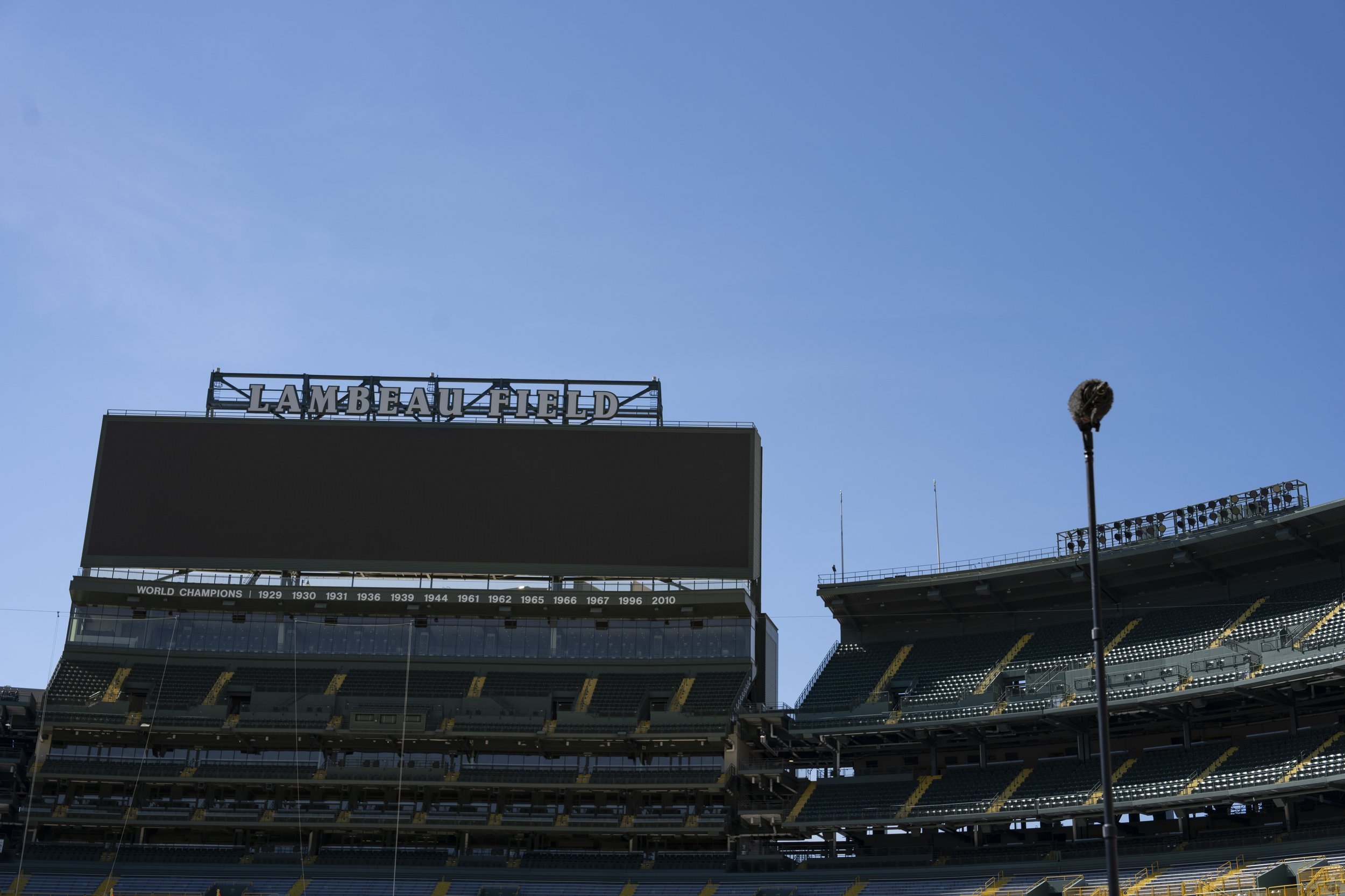 Empty Lambeau Field stadium under a clear blue sky with a scoreboard displaying 'Champions' and the years 1929 to 2010.