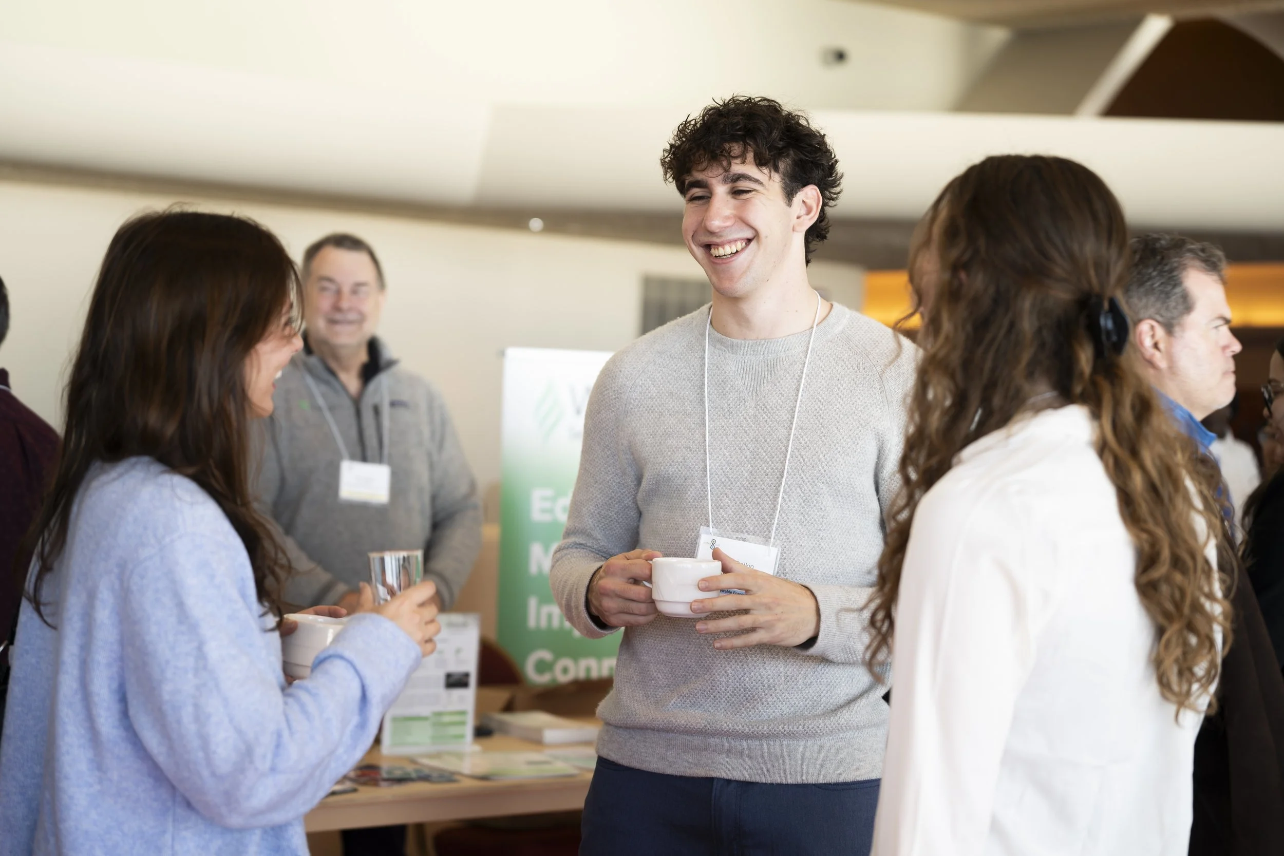 Group of people at a professional event, chatting and smiling, with conference badges, in an indoor setting.