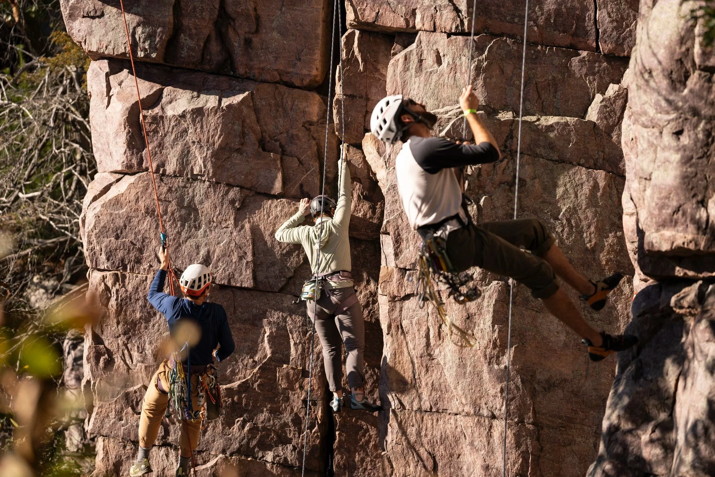 Three rock climbers on a quartzite rock, all wearing climbing gear and helmets.
