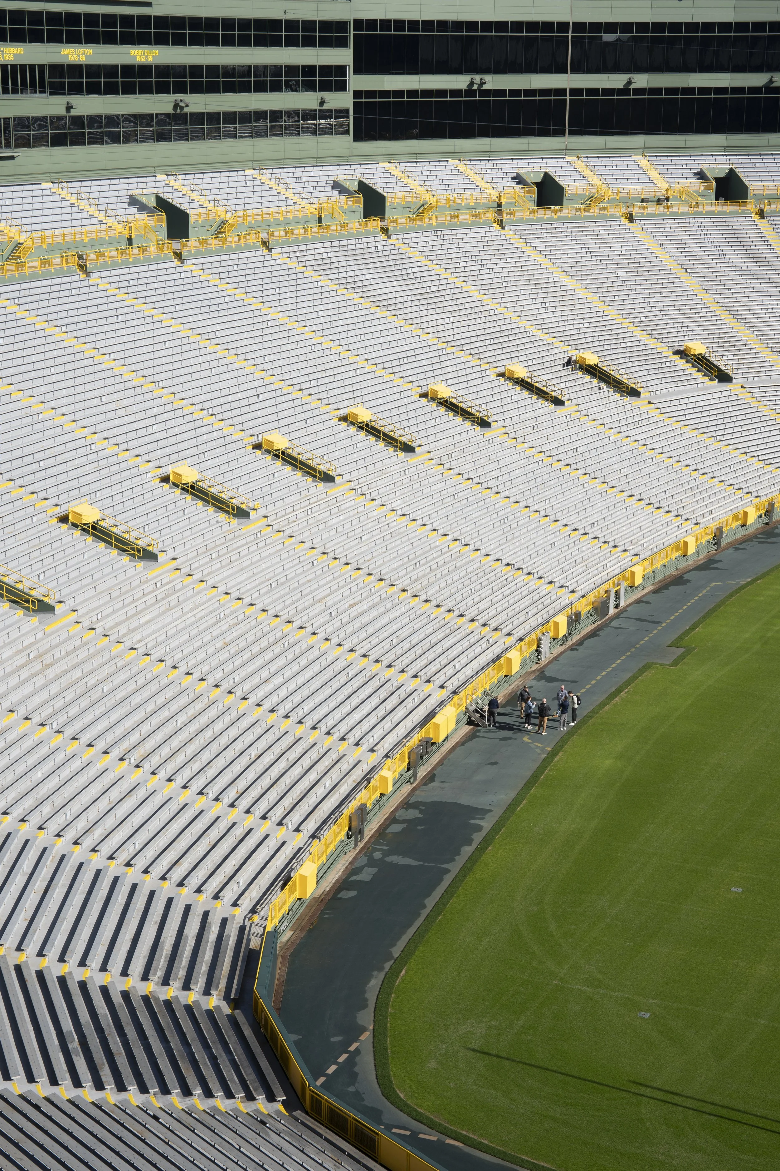 Empty stadium seats with a few people walking along the sideline of the field.