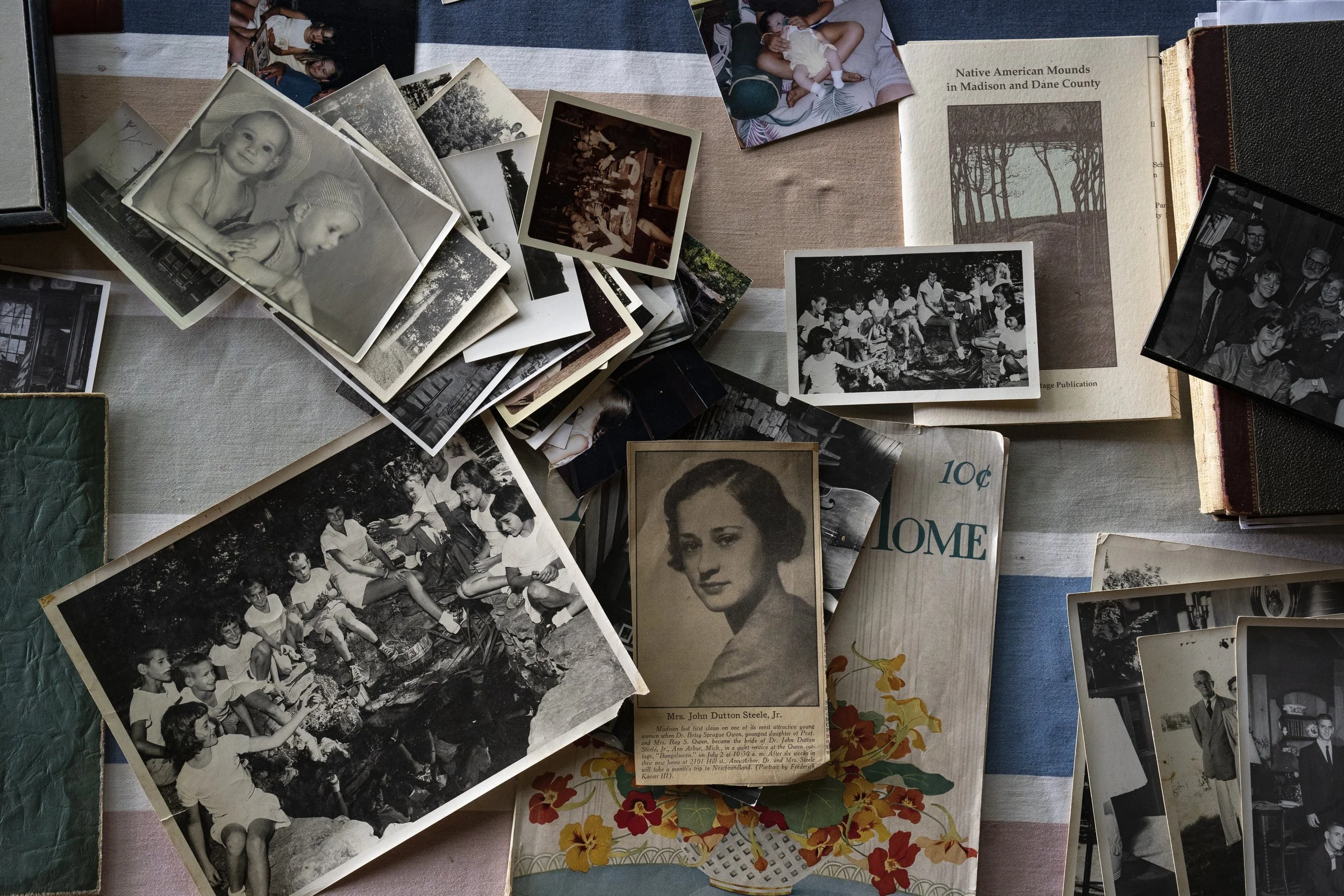 Collection of black and white and color photographs, some in old photo albums, scattered on a table. The photos depict various scenes, including children, group gatherings, and individual portraits.