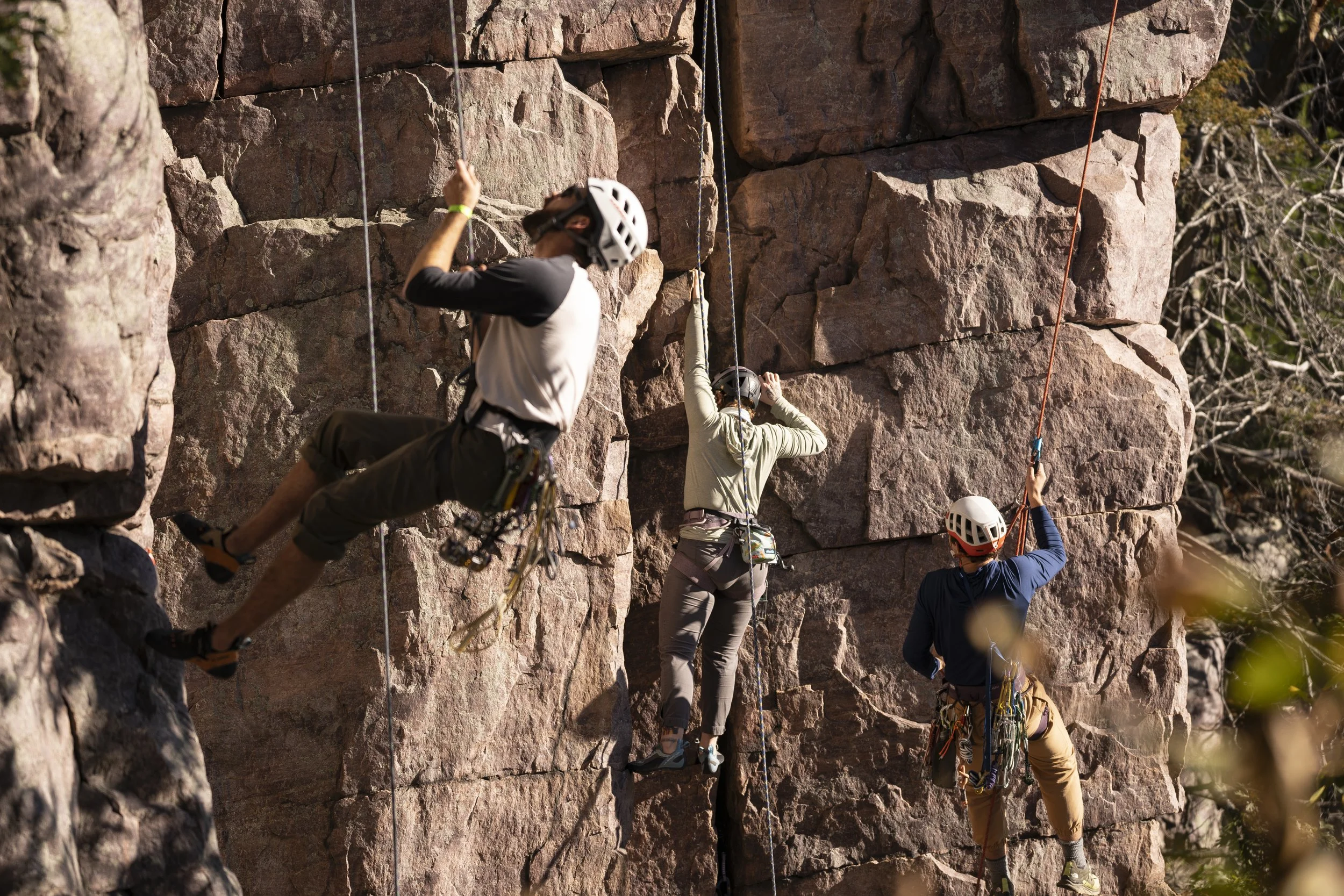 Three rock climbers securing themselves with ropes on a rugged cliff face during outdoor climbing.
