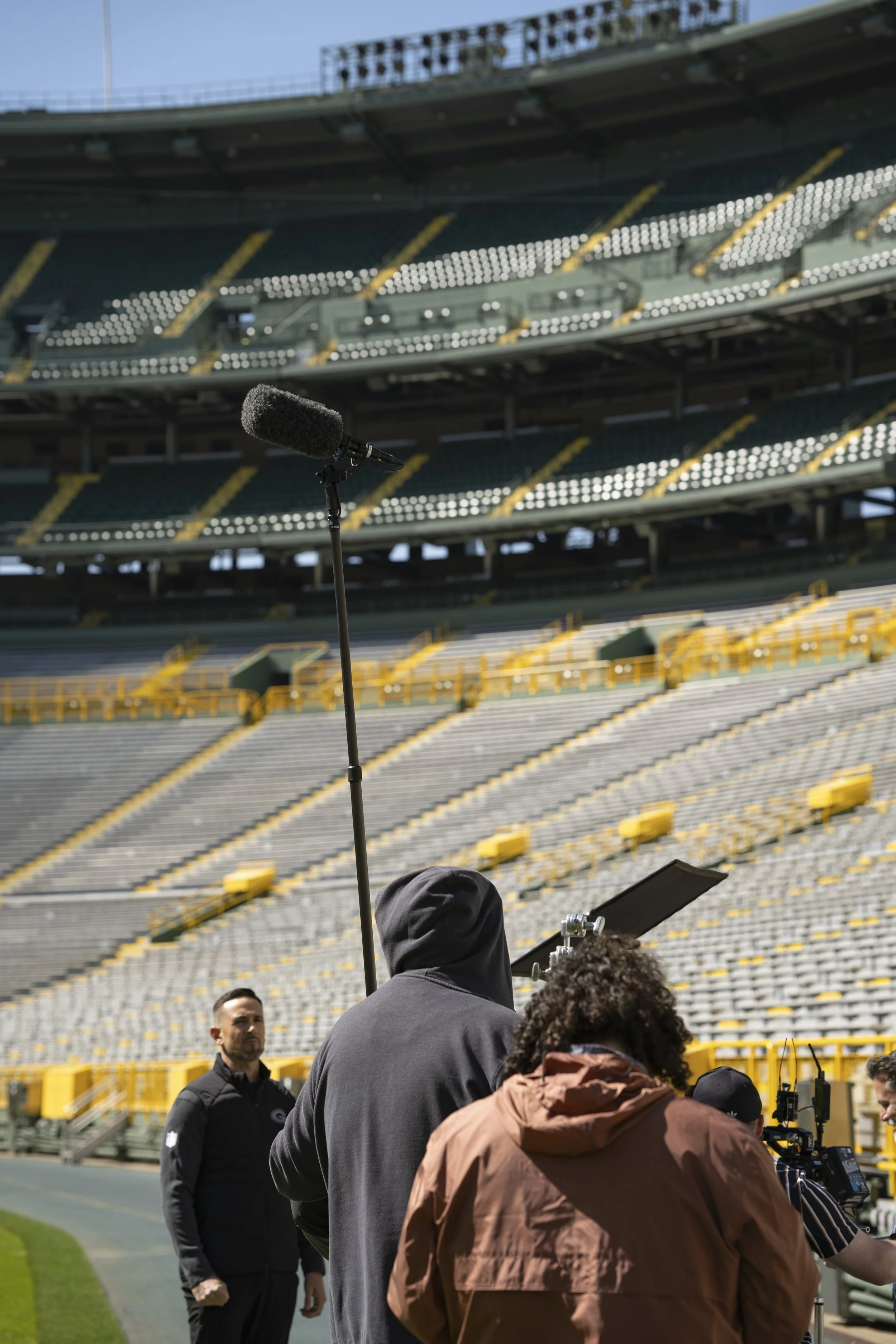 Film crew filming at a baseball stadium with empty seats in the background.