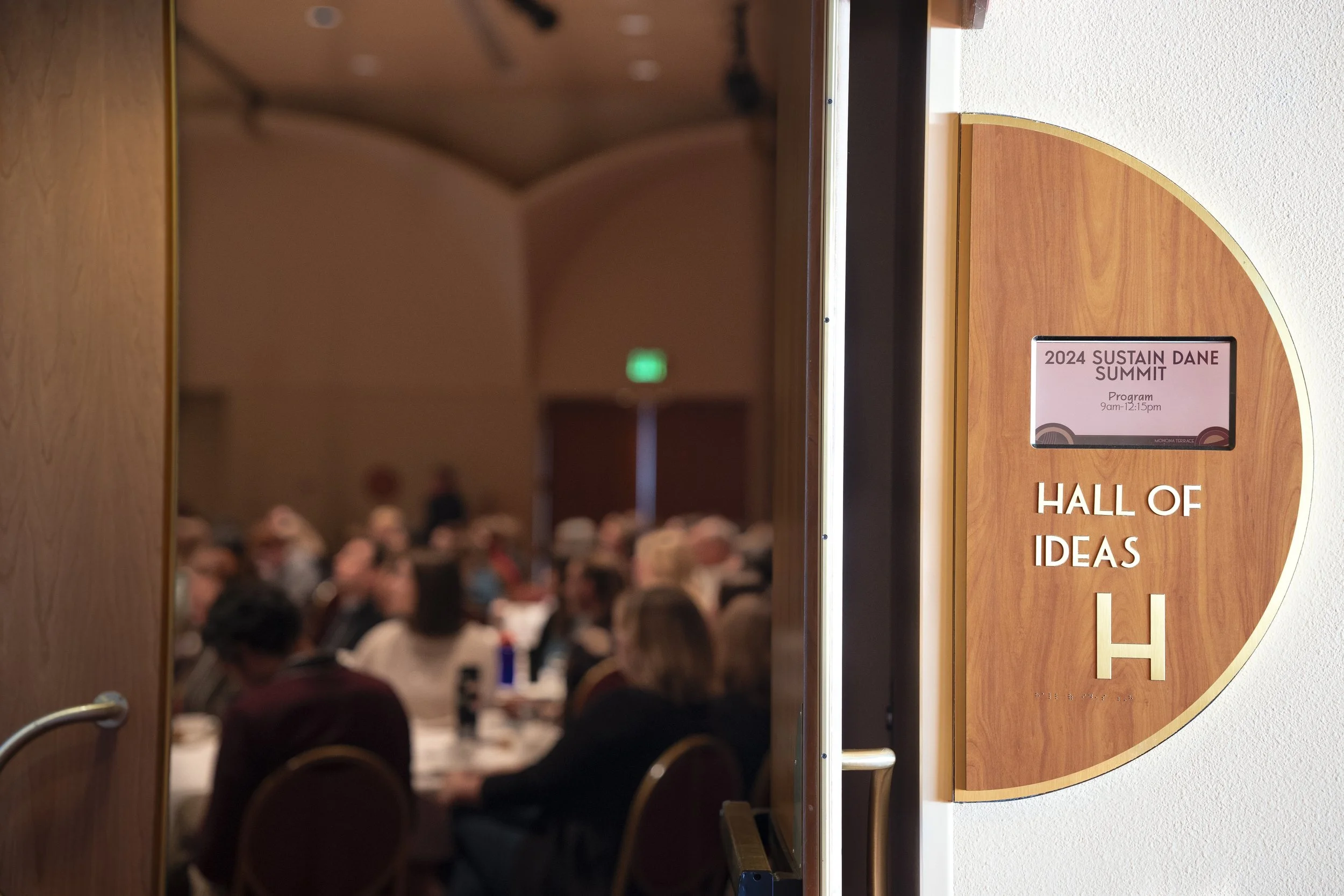Open door leading to a conference room filled with people attending the 2024 Sustain Dane Summit, located in the Hall of Ideas.