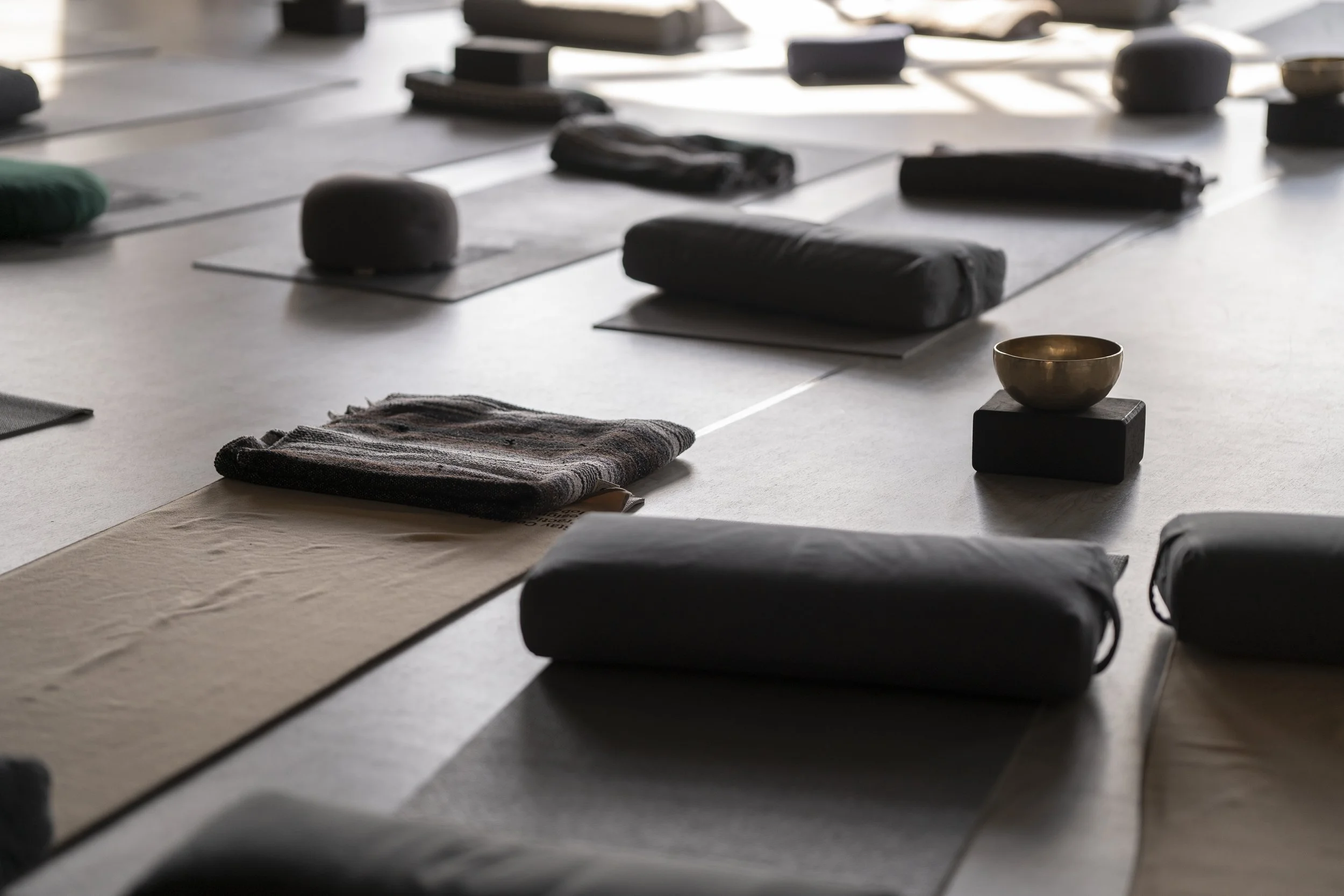 Yoga mats and meditation cushions arranged on the floor, with a singing bowl placed on a small black block.