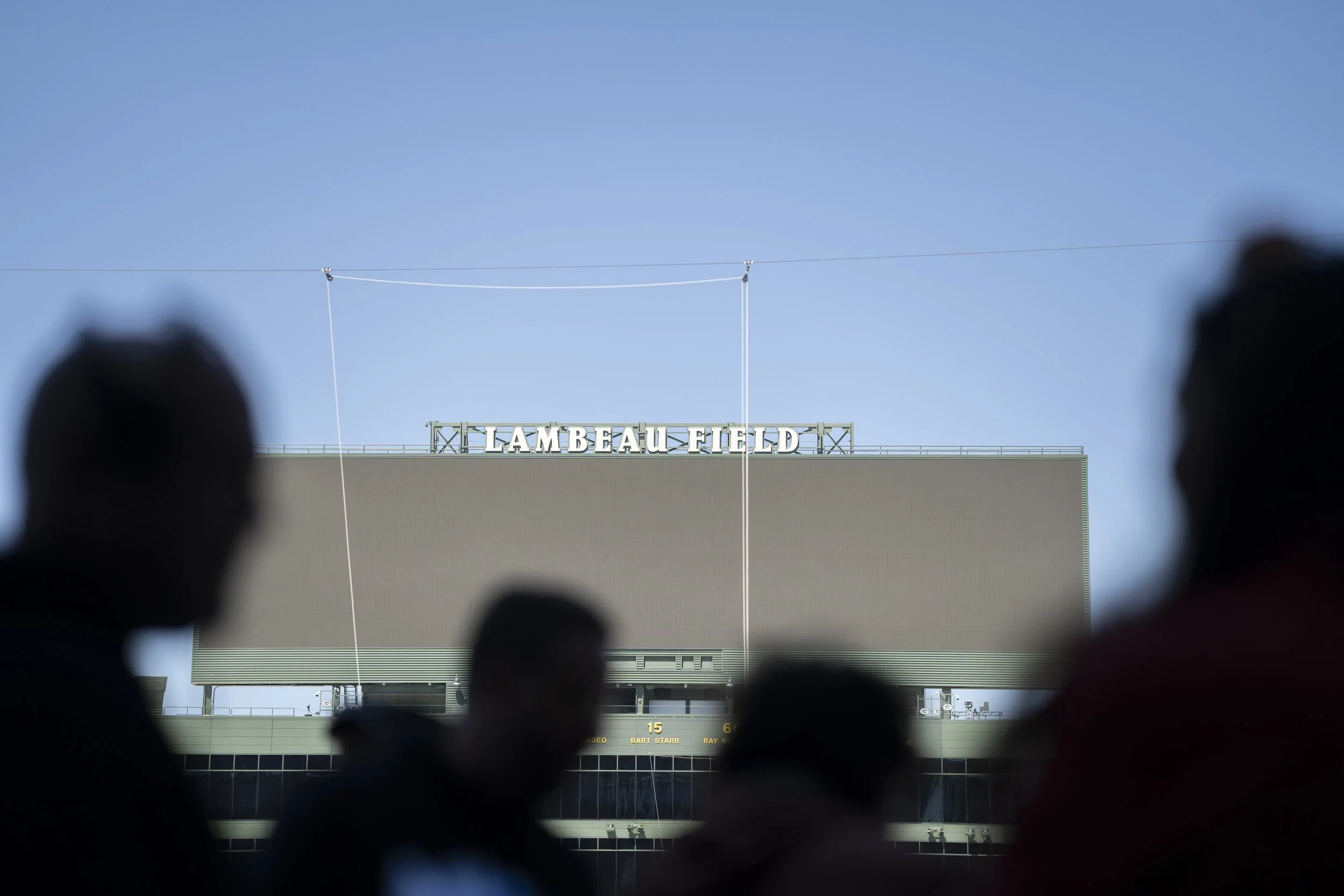 Silhouettes of people in front of Lambeau Field stadium with the sign visible on top of the building.