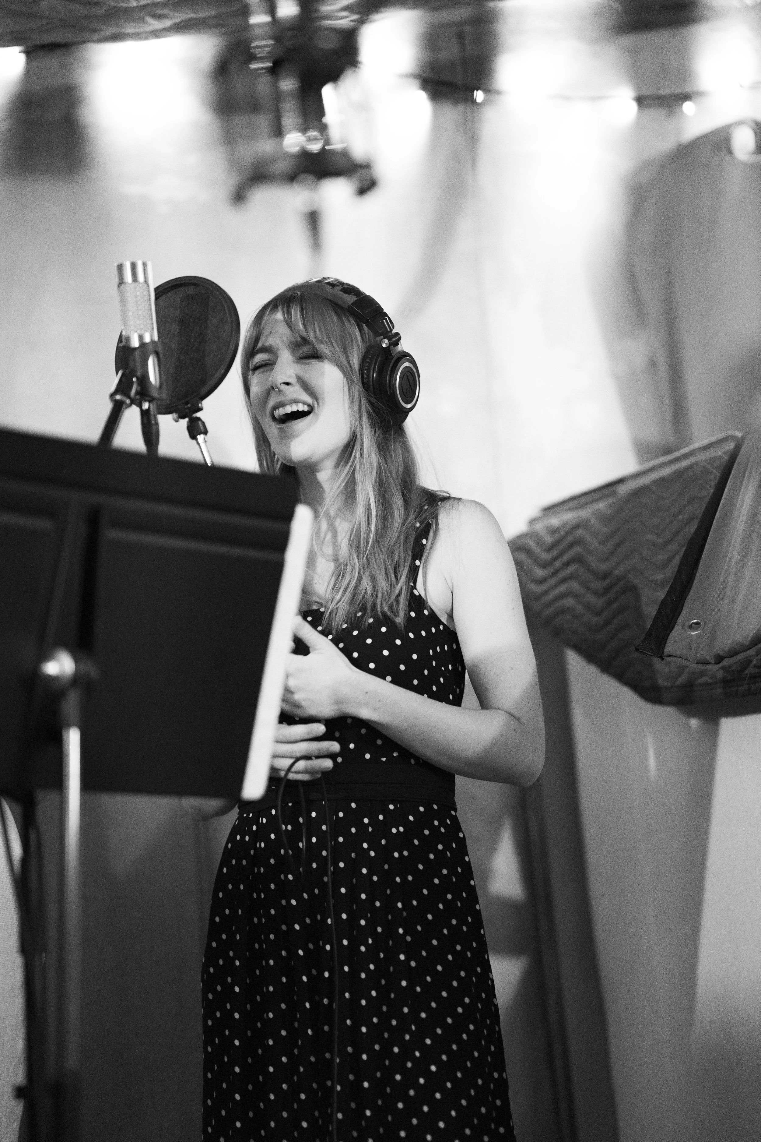 A woman in a polka dot dress singing into a microphone in a recording studio.