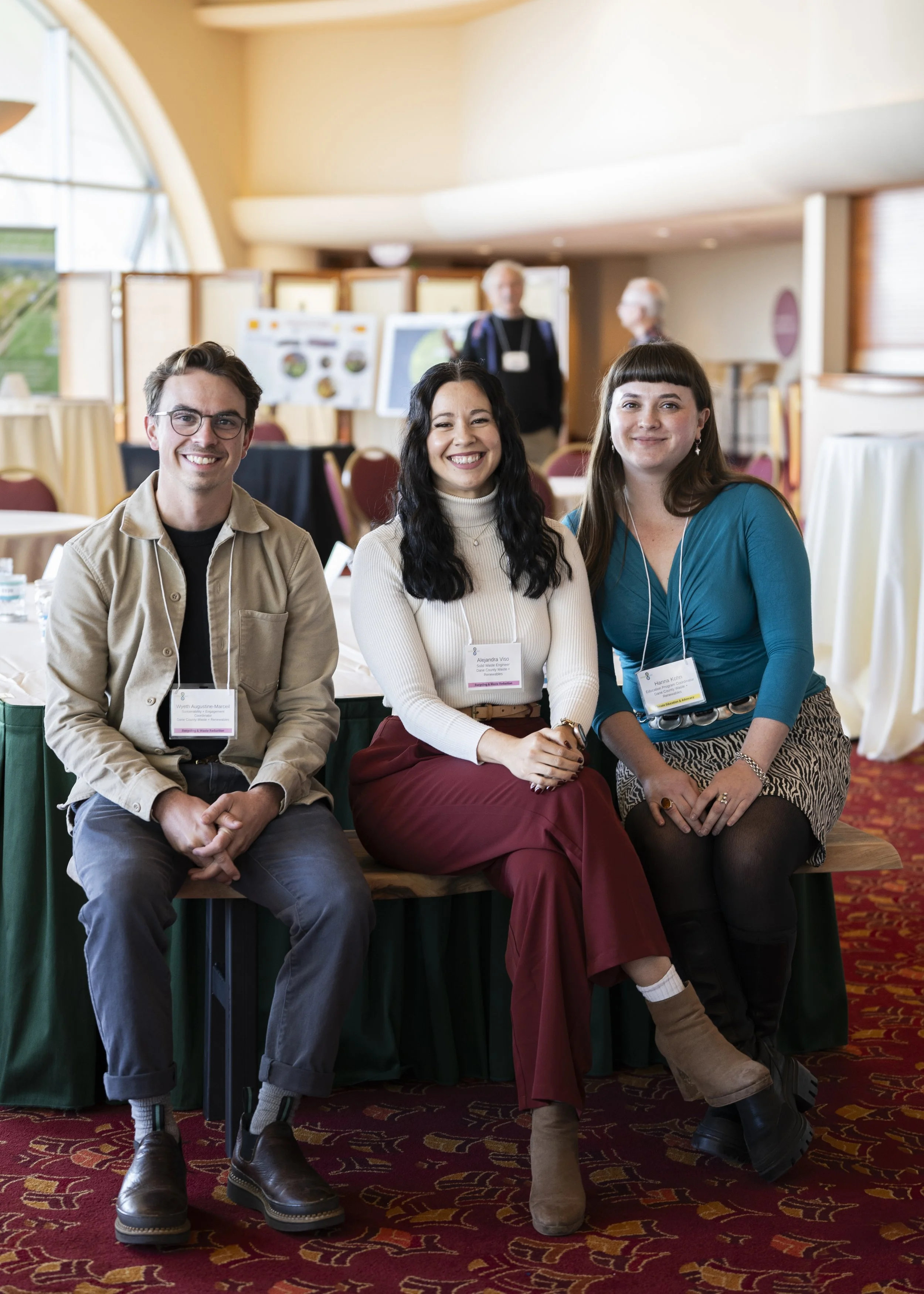 Three people sitting on a bench smiling at the camera in a conference room.