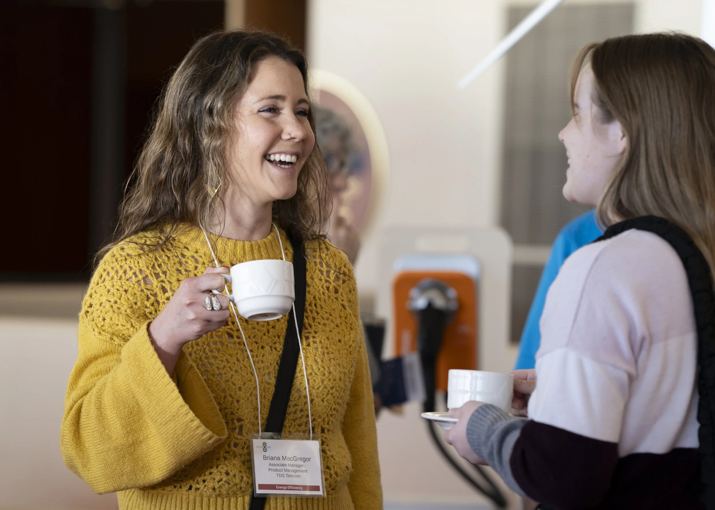 Two women smiling and engaging in conversation while holding coffee cups at a professional event
