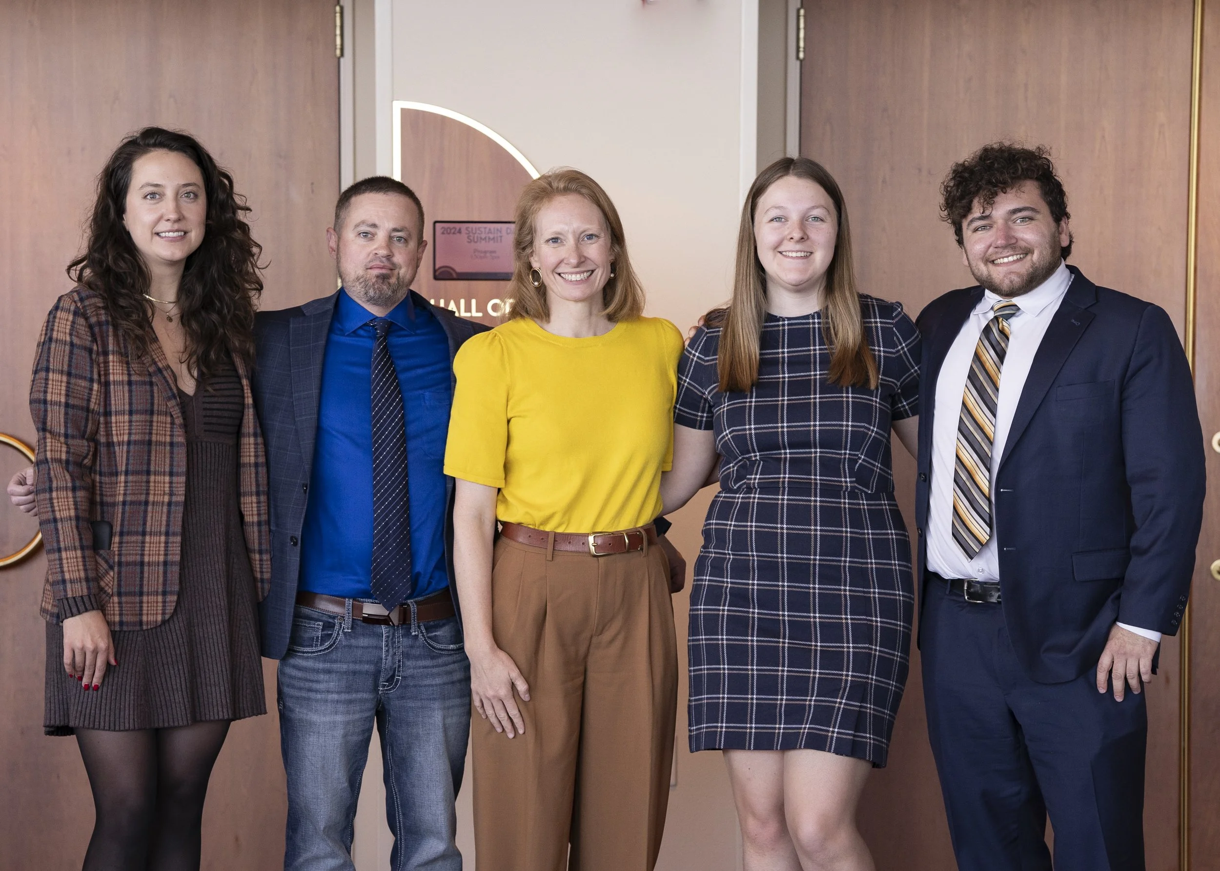 A group of five people standing together indoors, smiling for a photo at a professional event.